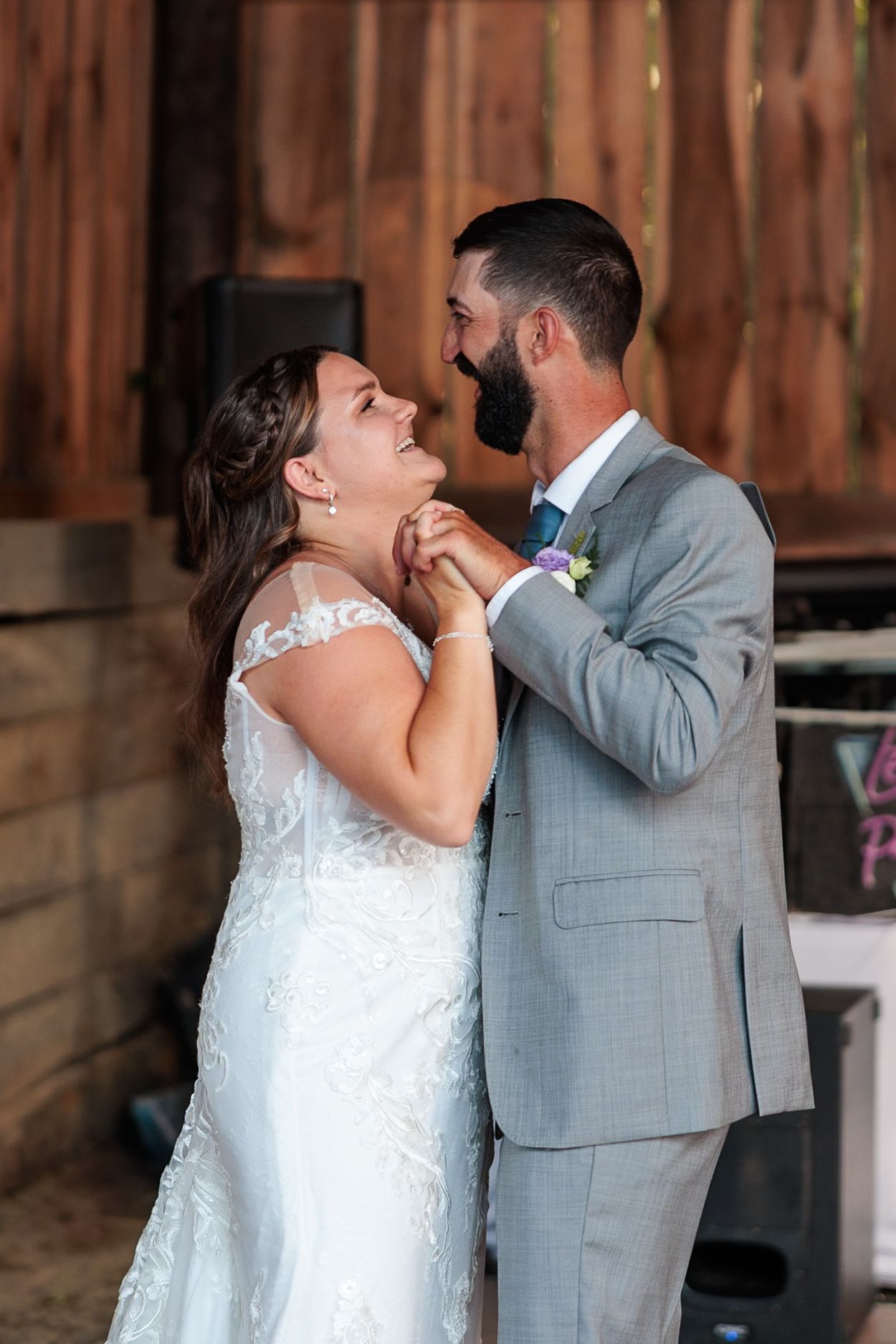 Bride and groom share a joyful first dance, laughing and holding hands in a rustic barn wedding venue.