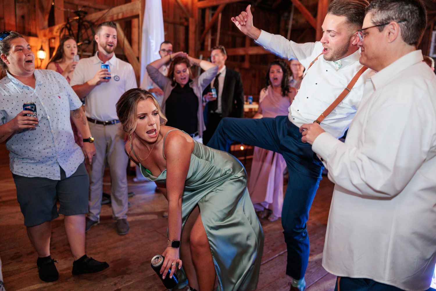 Wedding guests dancing and celebrating on a wooden dance floor in a rustic barn setting.