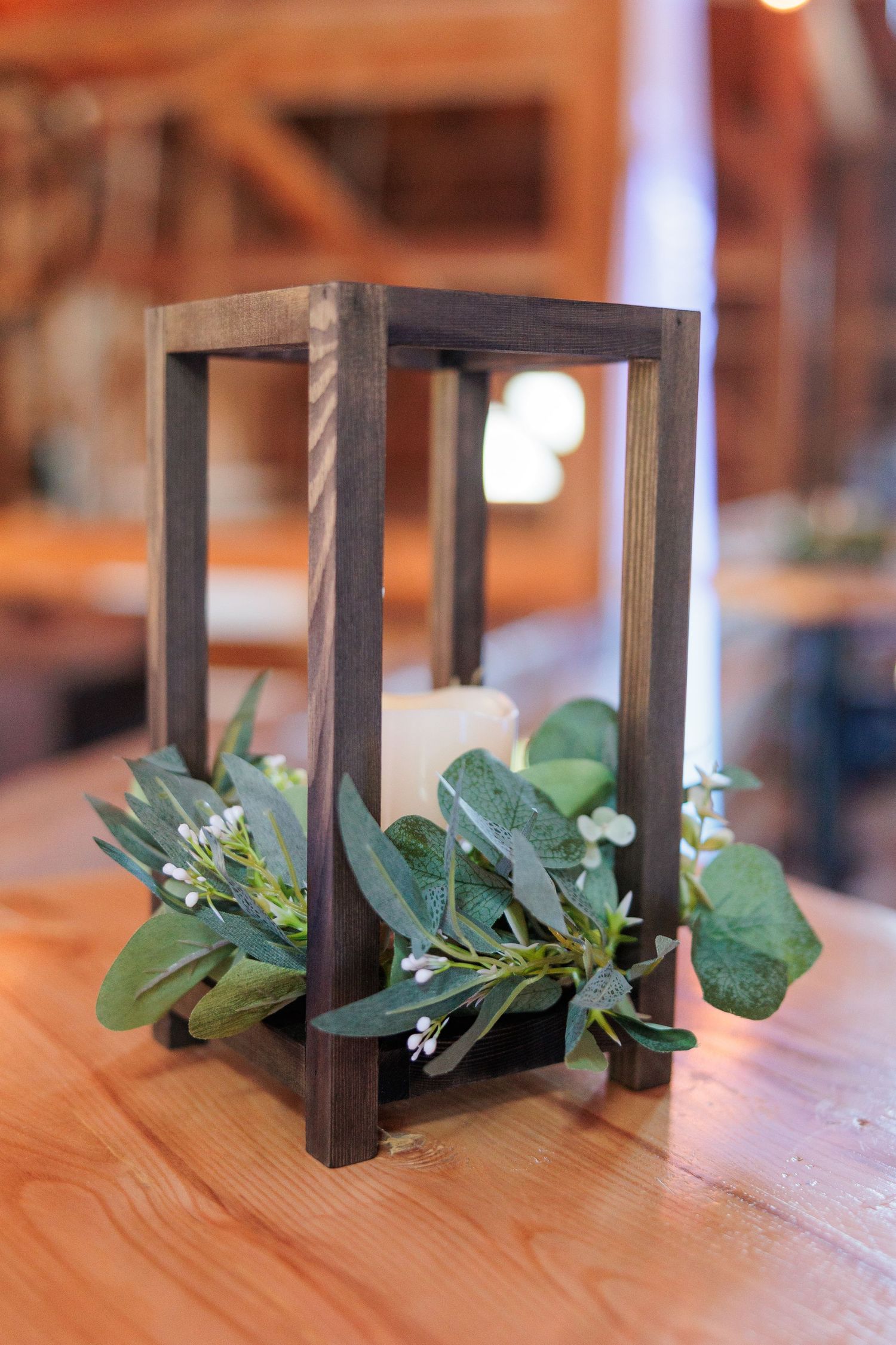 Wooden candle holders decorated with fresh greenery on rustic tables.