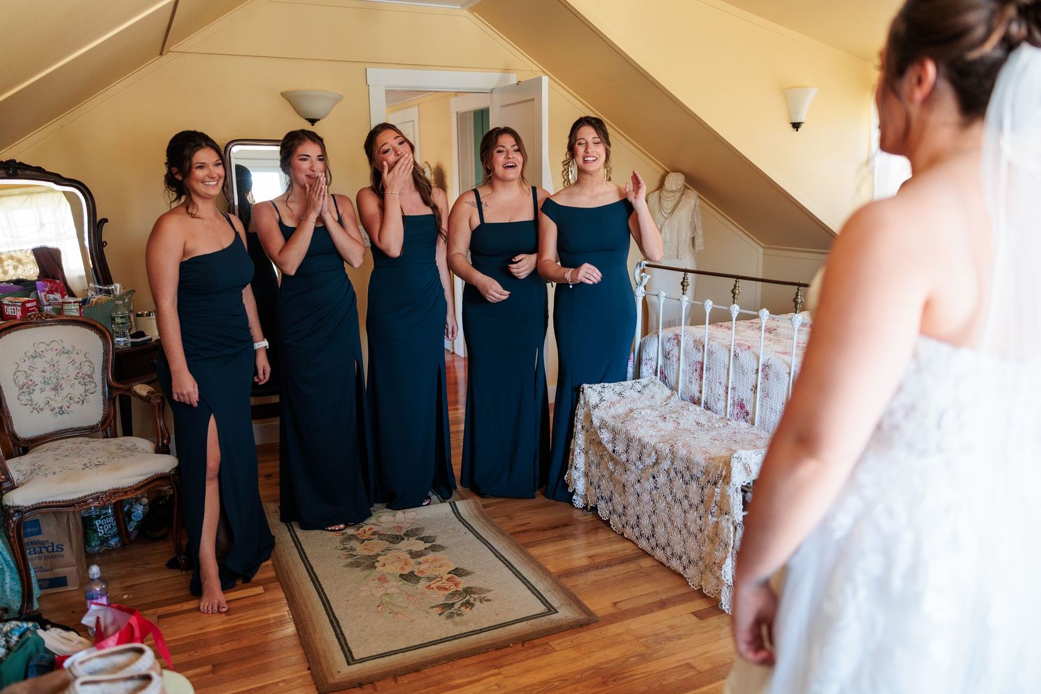 Wedding party members in navy dresses gather in a rustic room during pre-ceremony festivities.