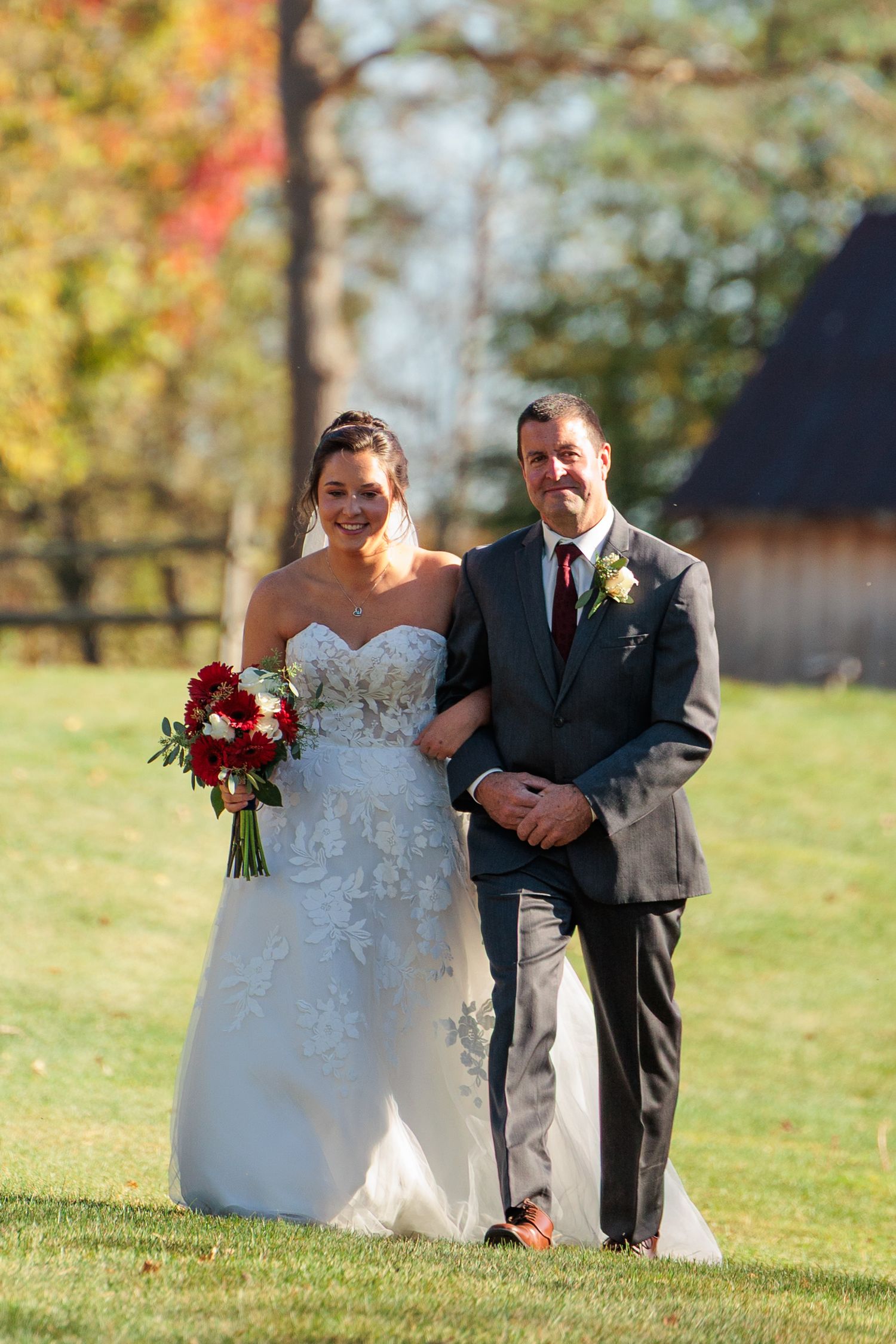 Wedding couple poses together on a lawn with autumn foliage in the background.