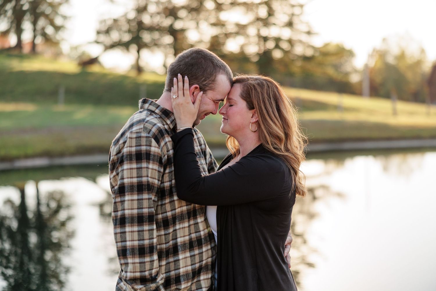 Couple touching foreheads romantically near a reflective pond during a golden hour engagement shoot.