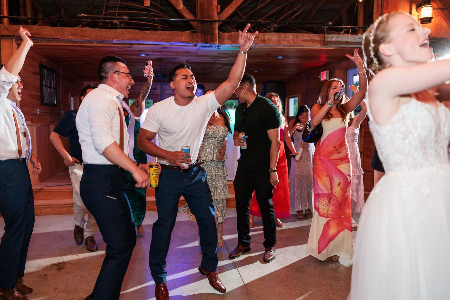 Energetic wedding guests dance and jump enthusiastically on the dance floor at a festive barn reception.