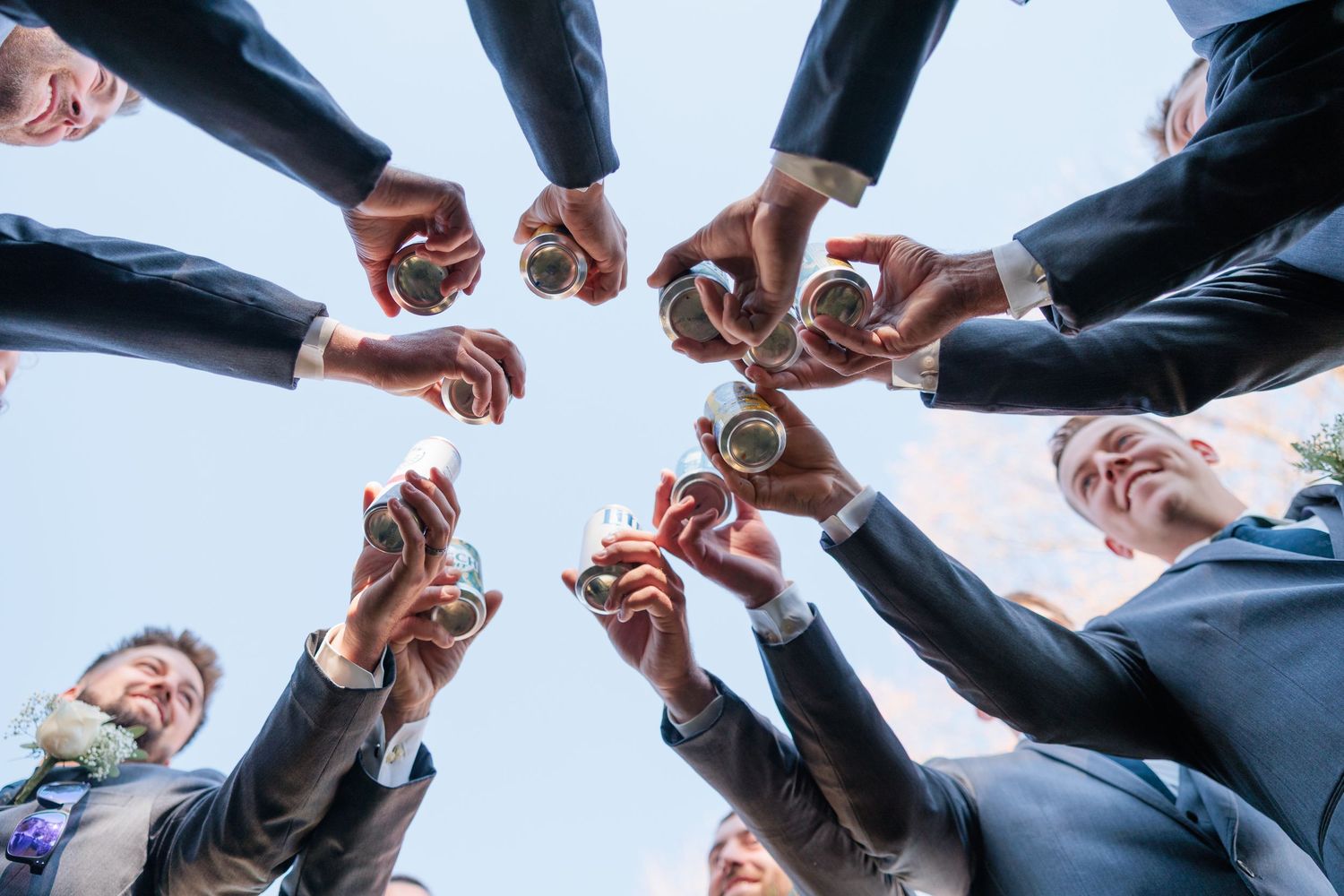 Group of groomsmen in dark suits toasting drinks in circle formation.
