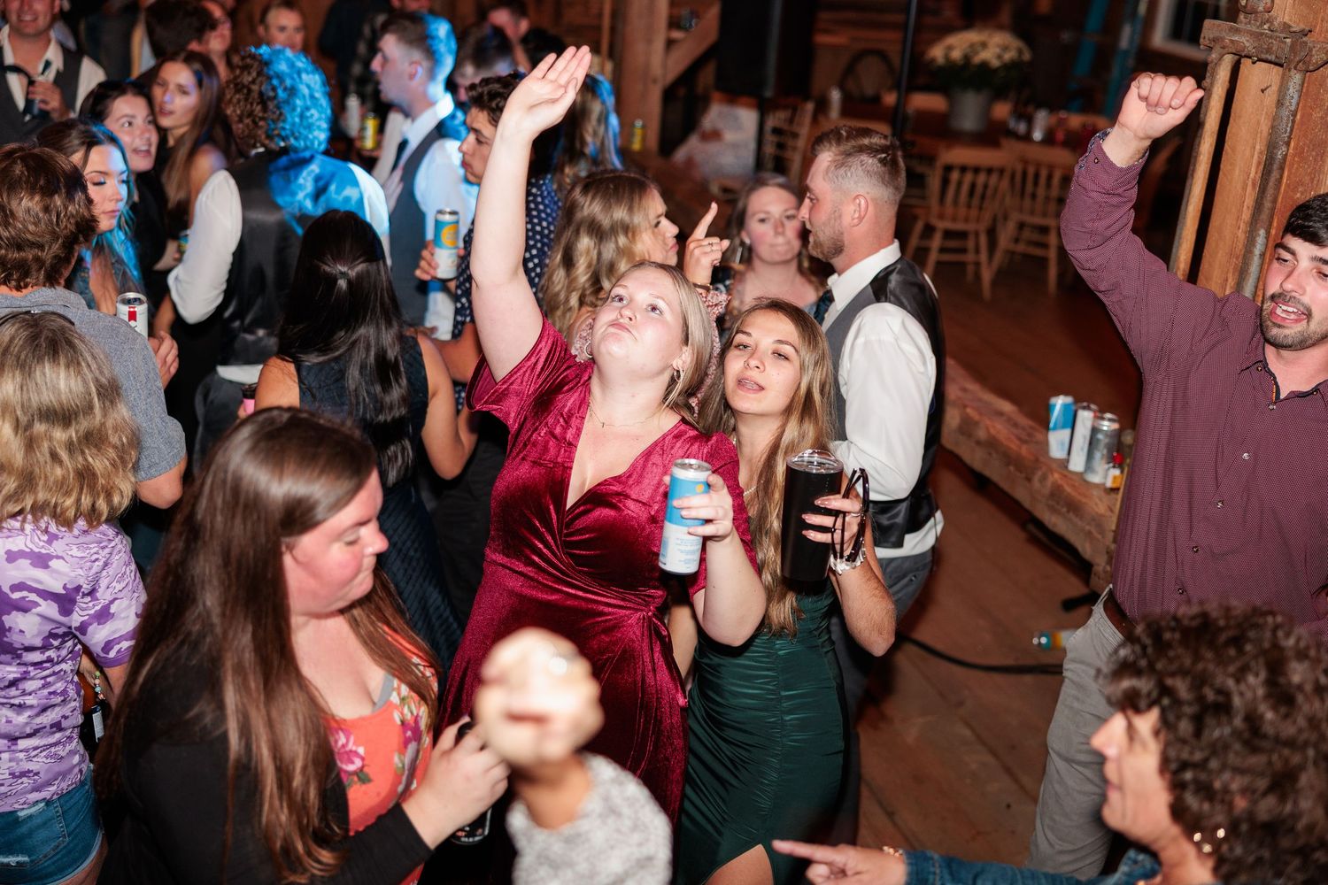 Energetic wedding reception celebration with guests dancing and raising drinks in a rustic venue.
