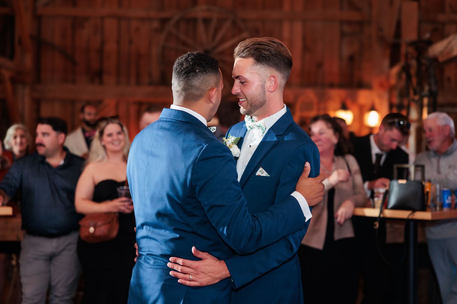 Wedding guests dance together in a rustic barn venue with warm lighting.