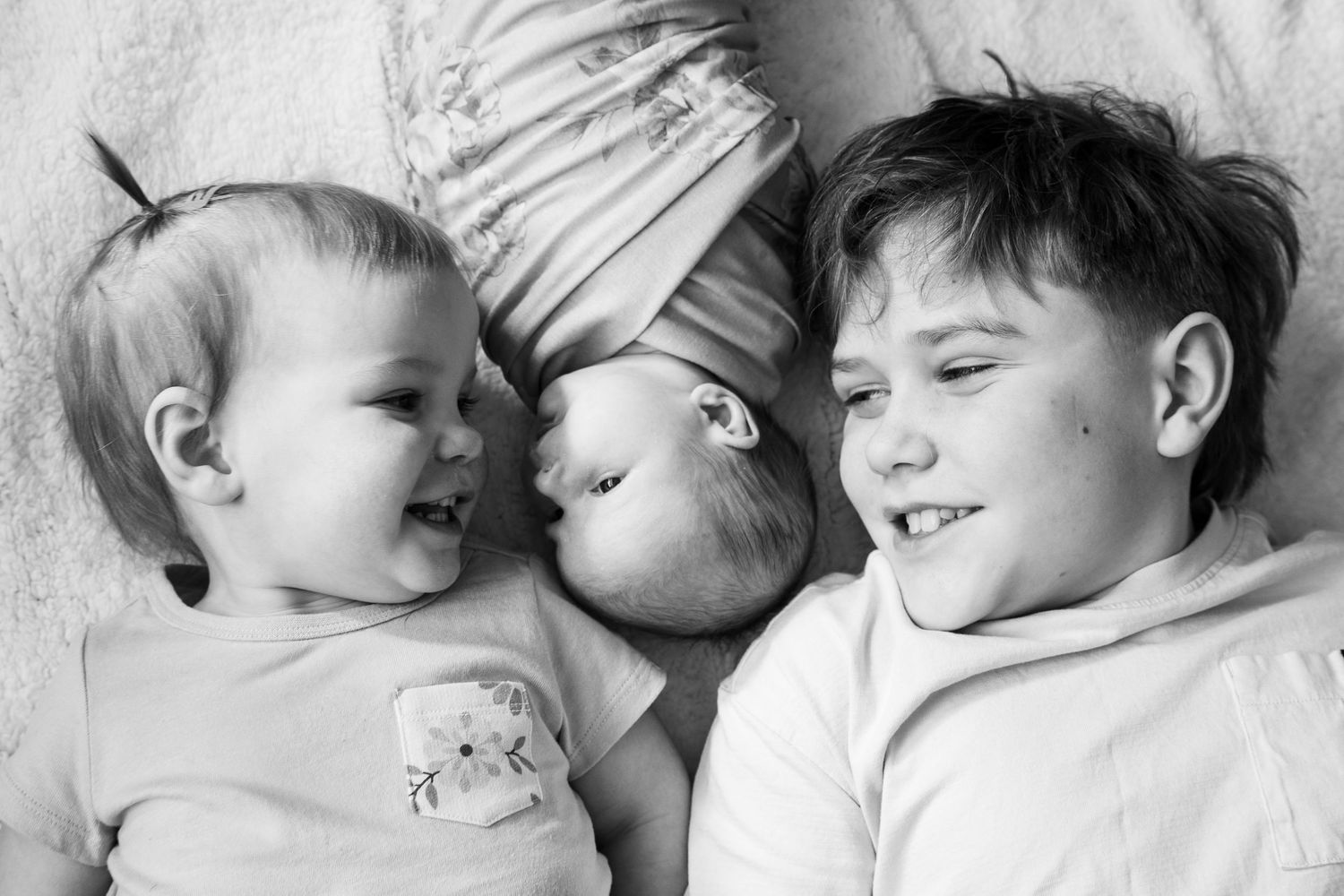 Black and white photo of three siblings lying together, including a newborn baby in the middle.