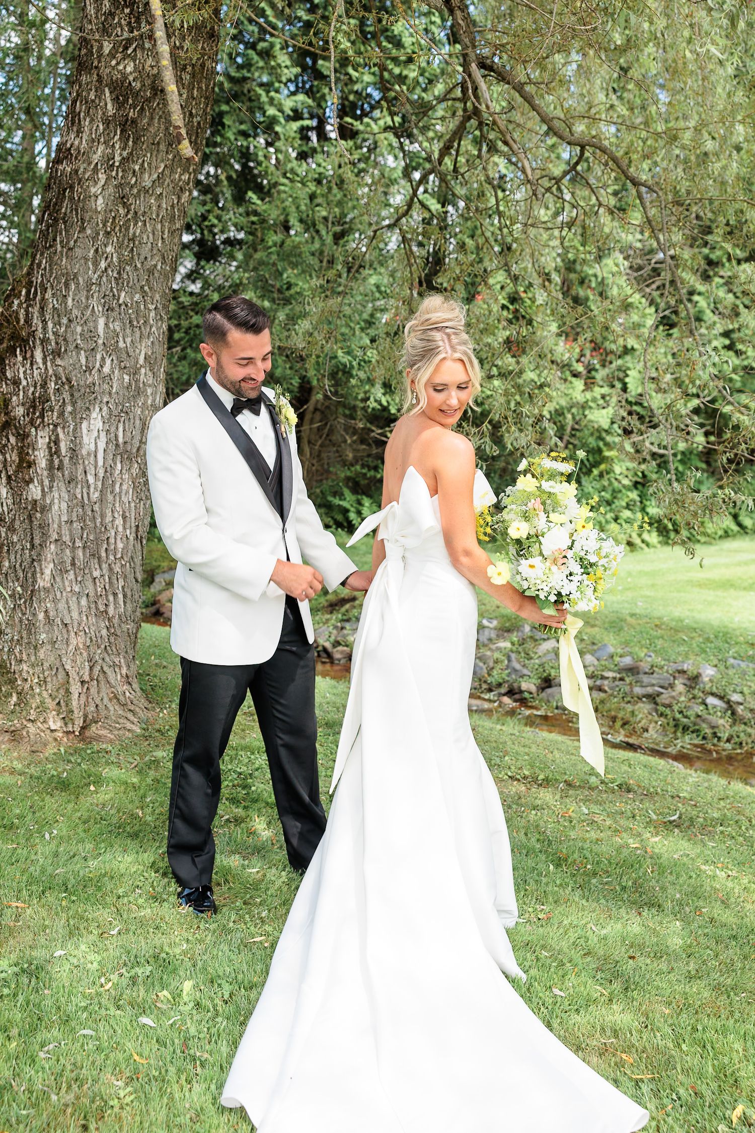 Bride and groom sharing a first look moment under a large tree in a lush green garden setting.