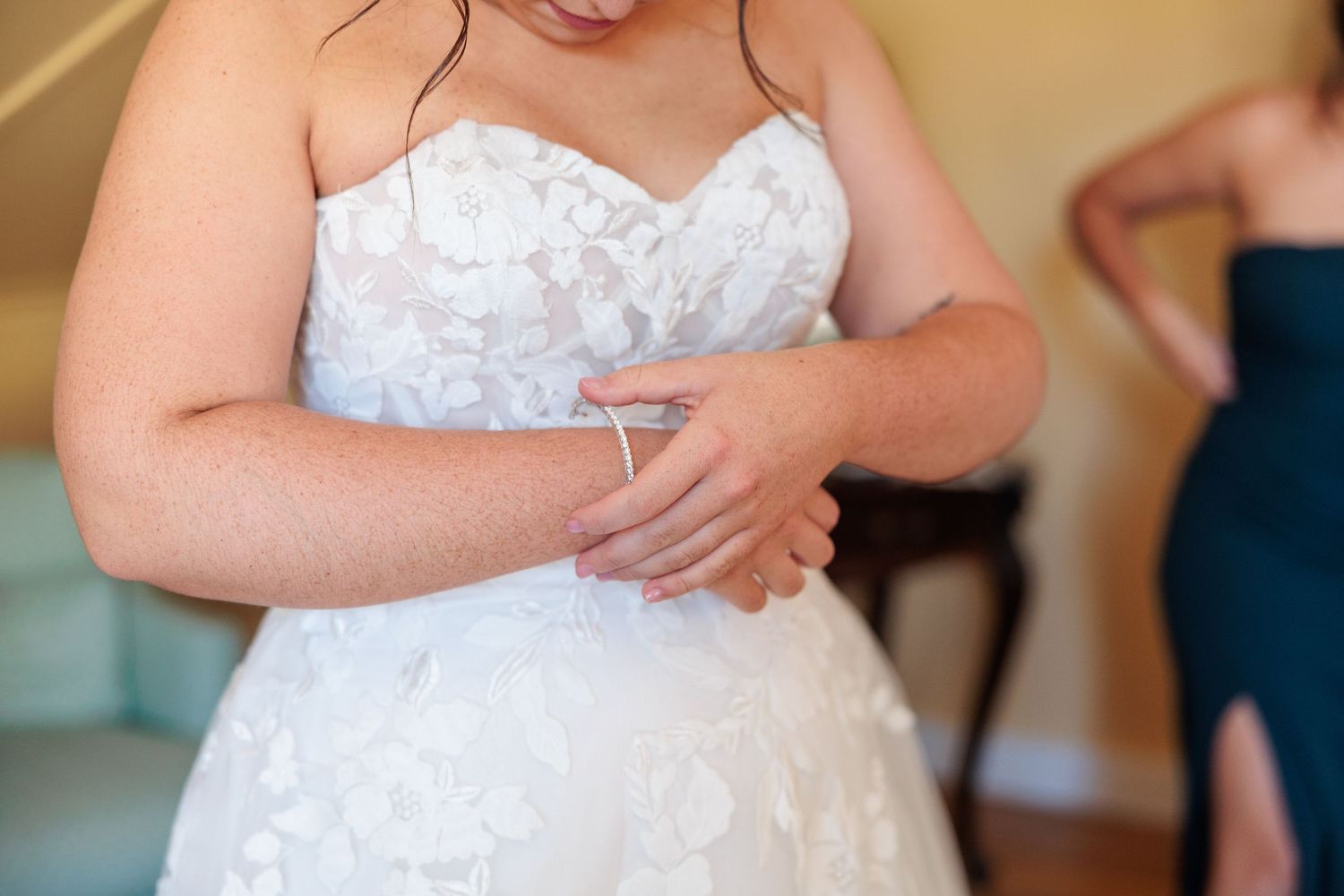 Bridesmaids in navy blue dresses gather around a bride in a white lace gown during wedding preparations.