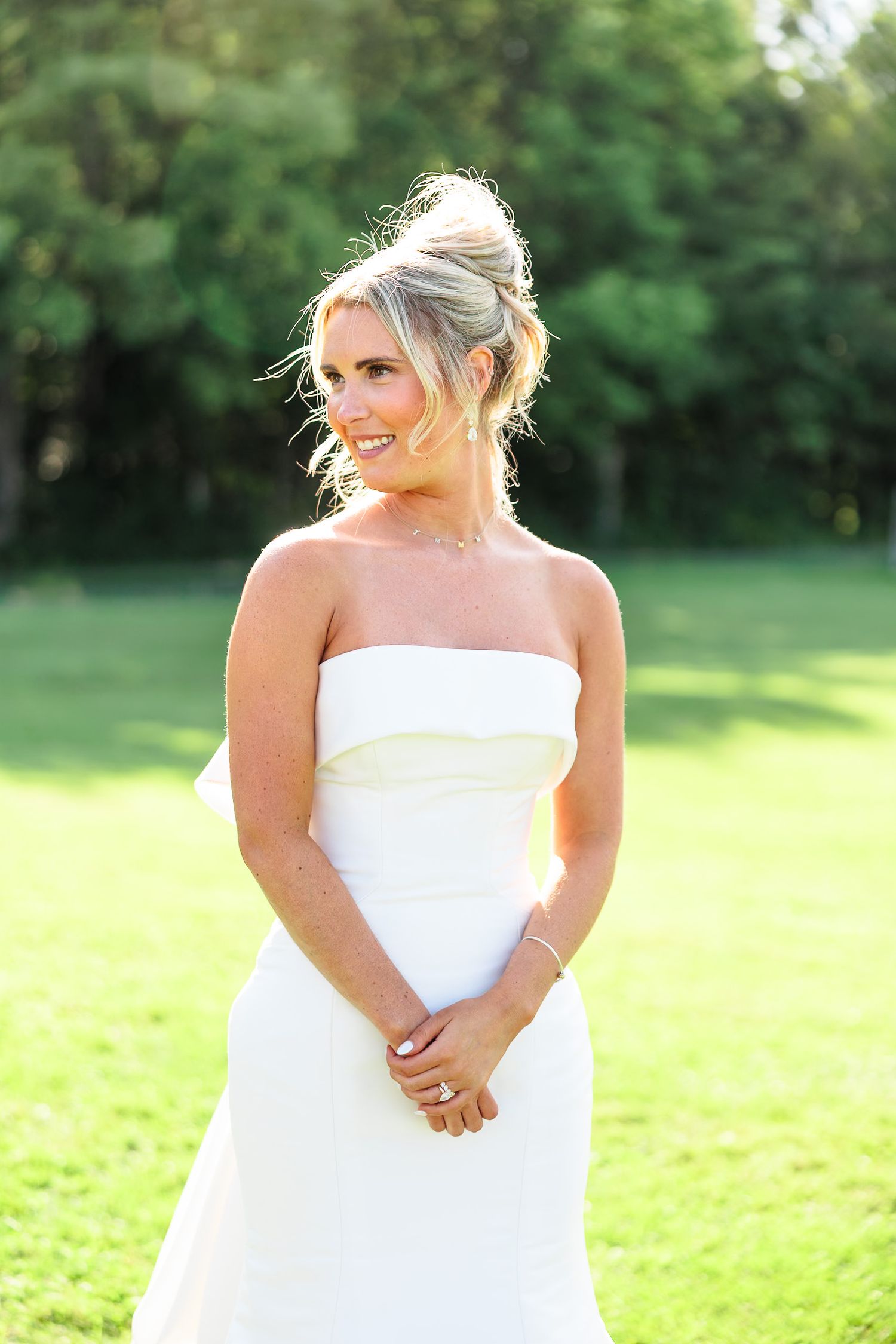 Elegant bride in strapless white wedding gown smiles joyfully during sunny outdoor bridal portrait.