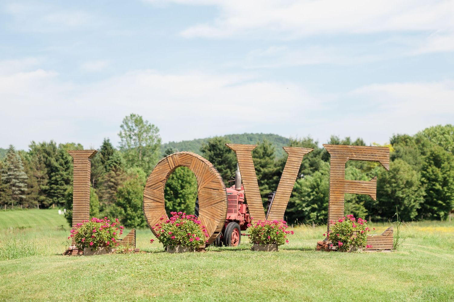 Large LOVE letters made of hay bales with a red tractor and flower arrangements in an outdoor field.