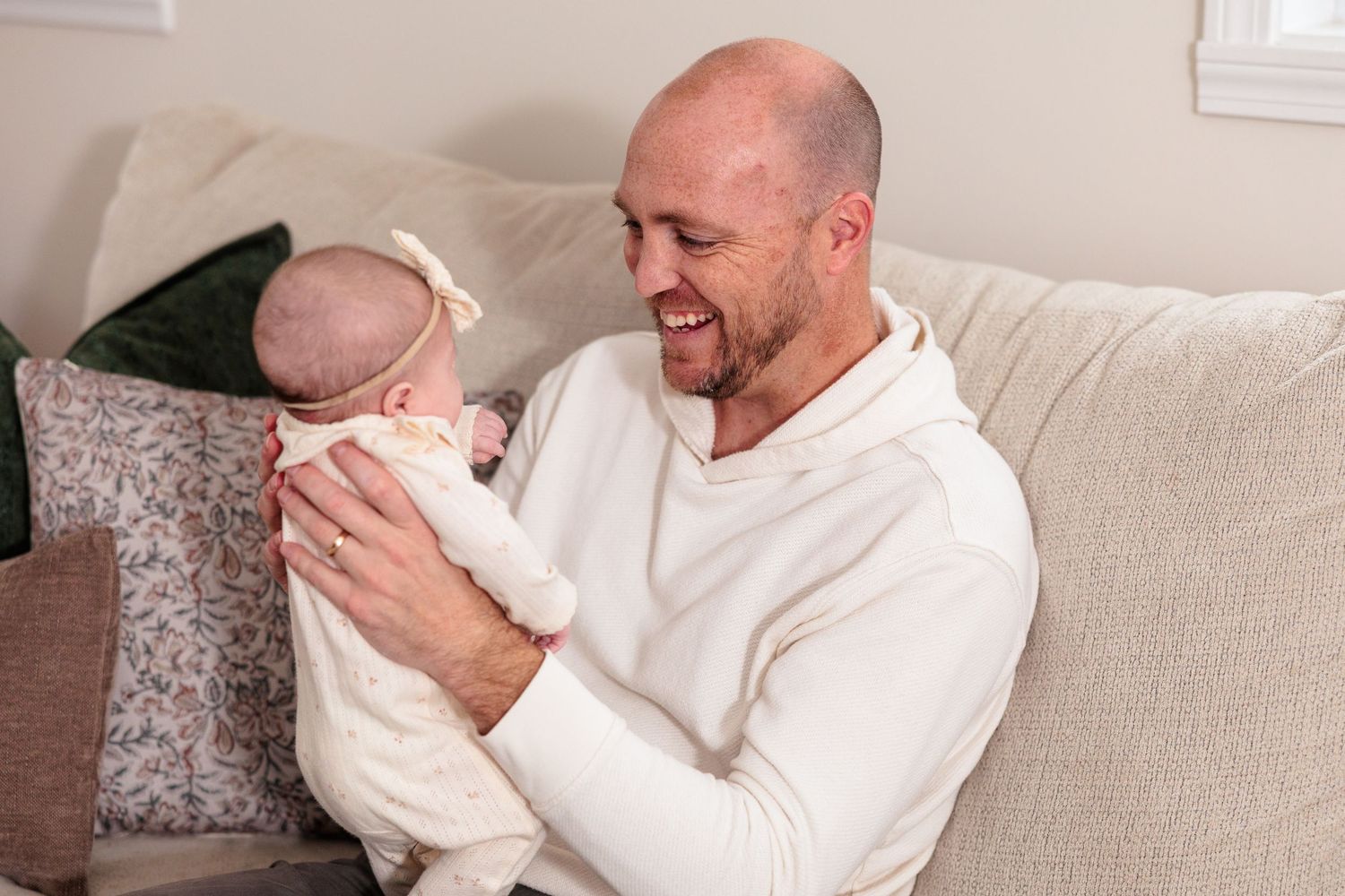 Adult in white sweater sitting on couch sharing joyful moment with infant in casual home setting.
