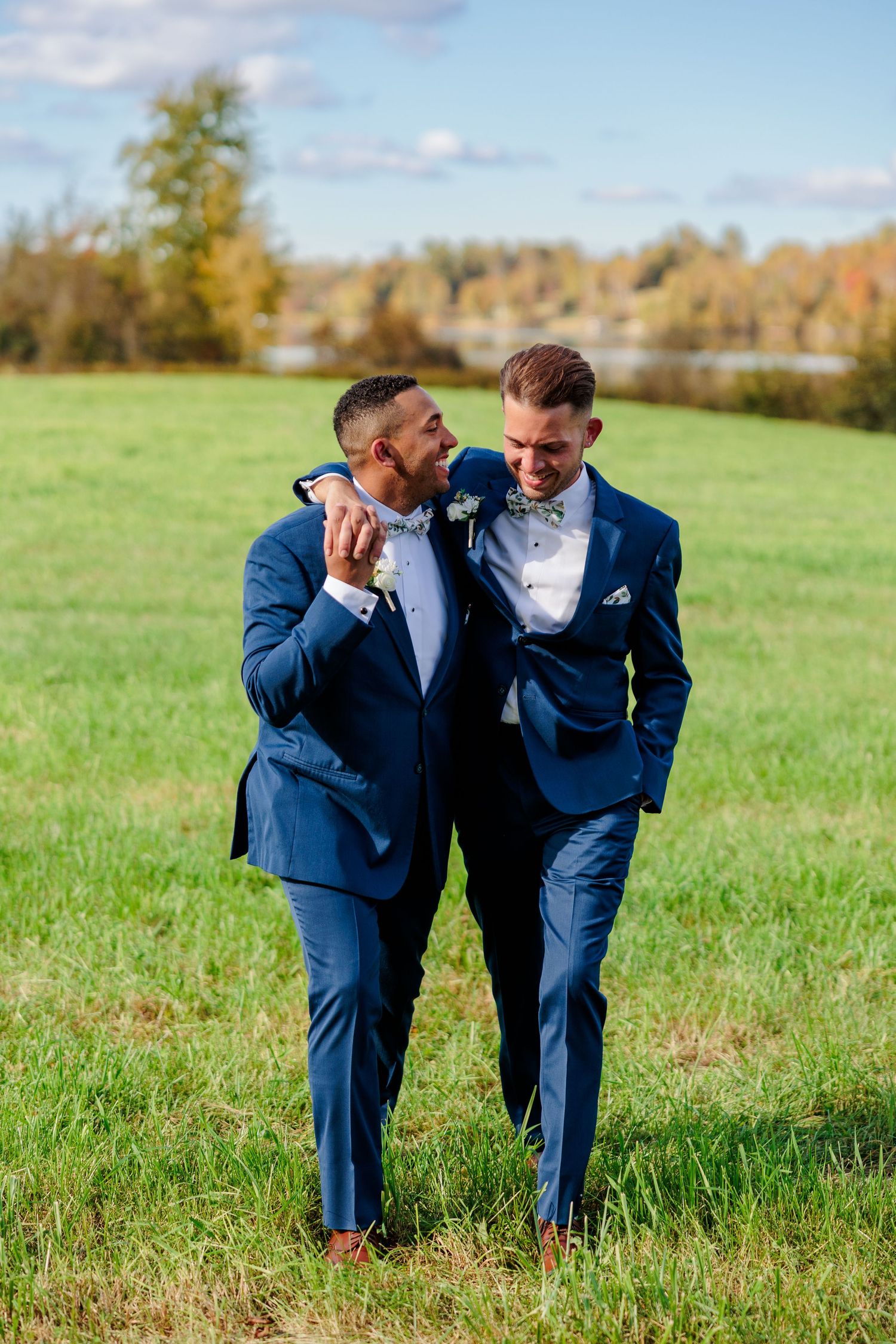 Couple laughing together in matching navy suits on sunny autumn meadow.