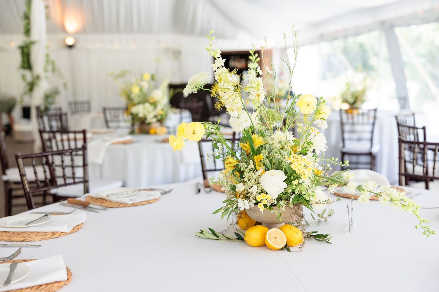 Elegant wedding reception table with yellow and white floral centerpiece featuring lemons under a white tent.