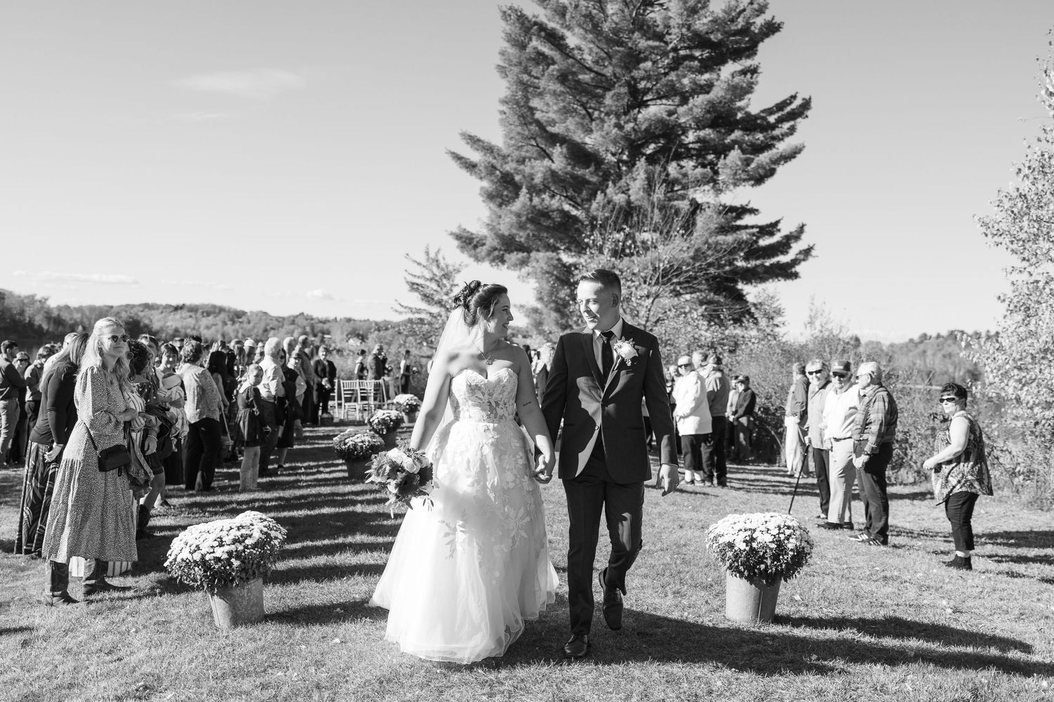 Black and white photo of newlyweds walking back down the aisle after outdoor fall ceremony.