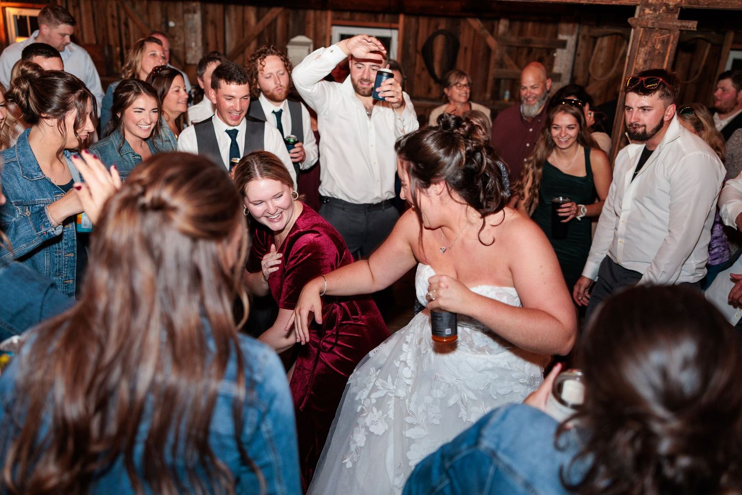 Bride in white lace gown dances joyfully with guests at a festive wedding reception celebration.