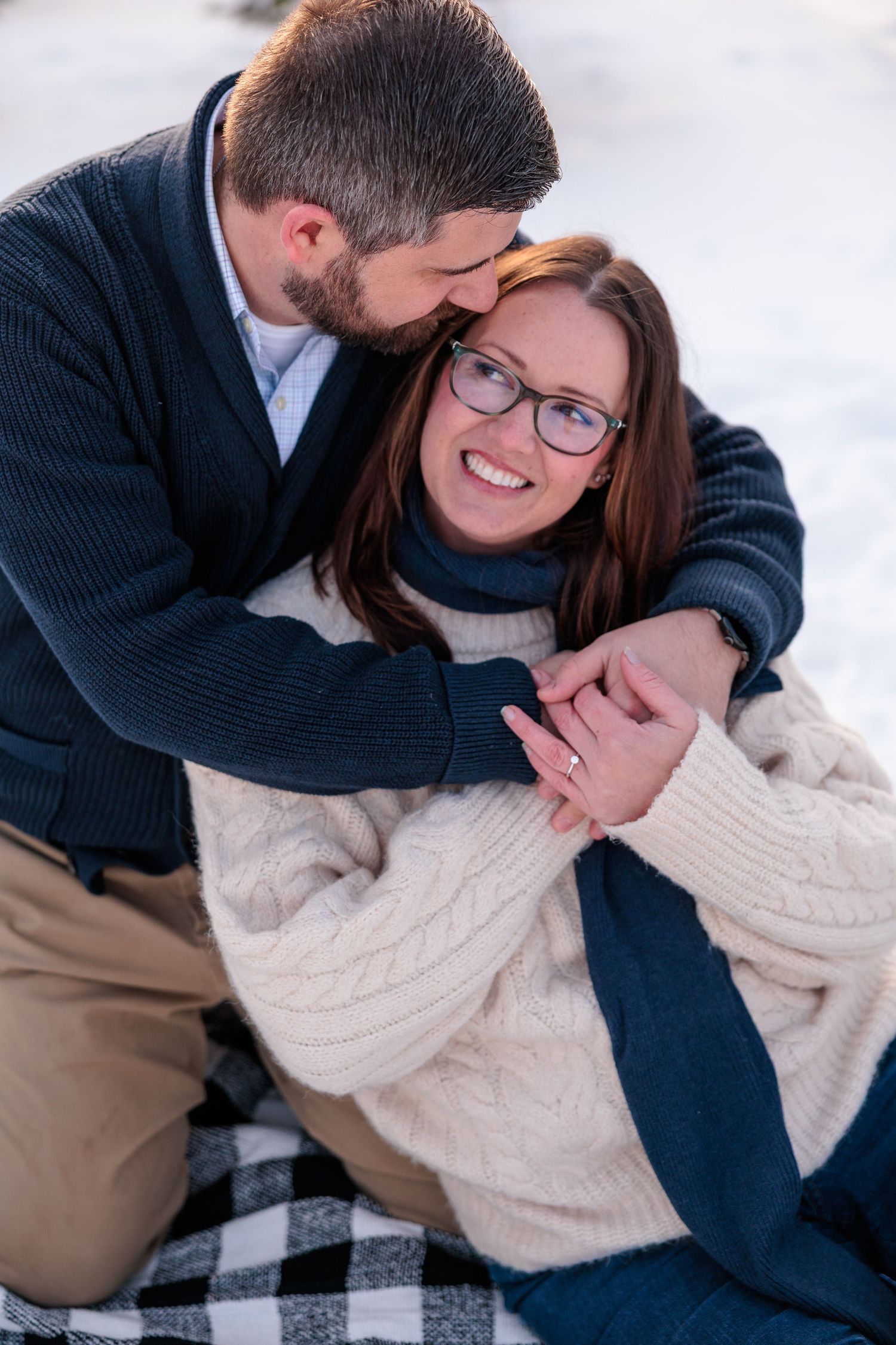 Man kissing woman on forehead while embracing her on a snowy winter day outdoors.
