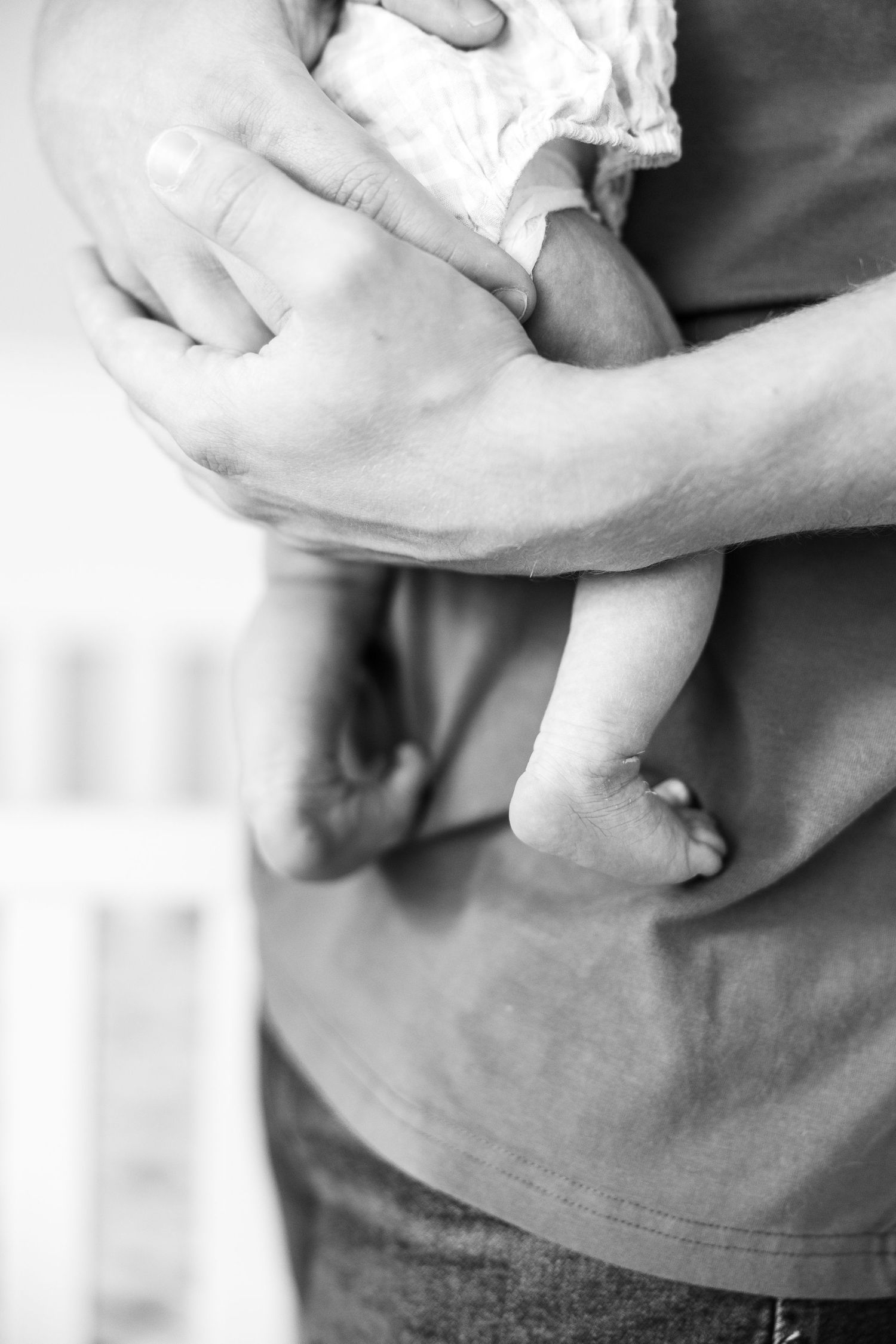 Close-up black and white photo of a father cradling a newborn baby against his chest.