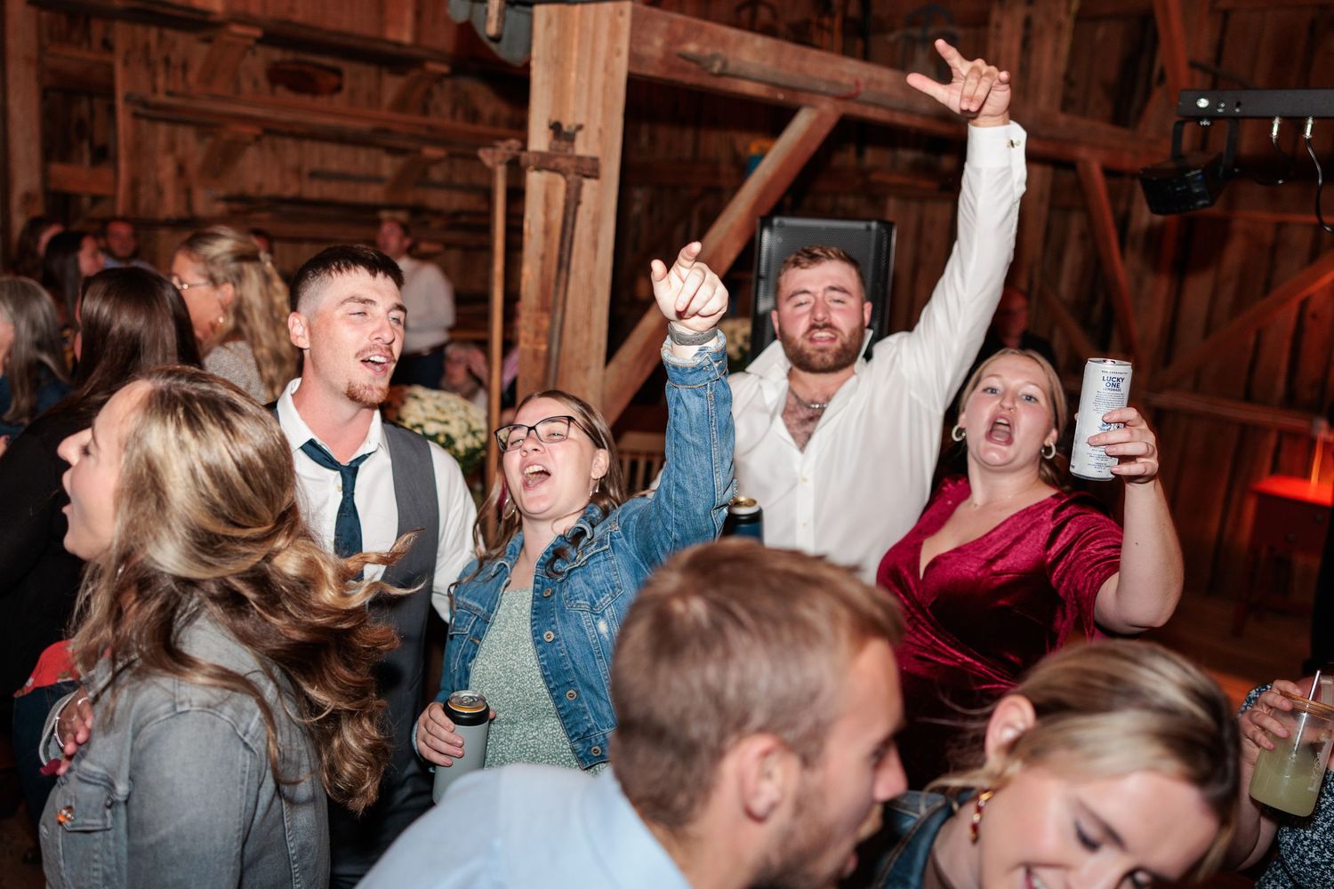 Excited wedding guests dance and celebrate enthusiastically in a rustic barn reception venue.
