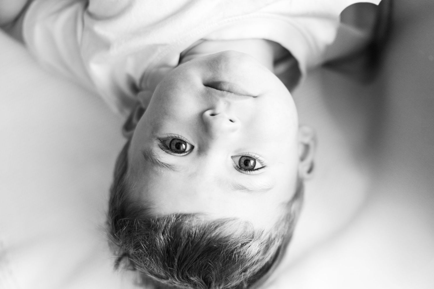 Black and white overhead portrait of a smiling toddler boy looking up at the camera.