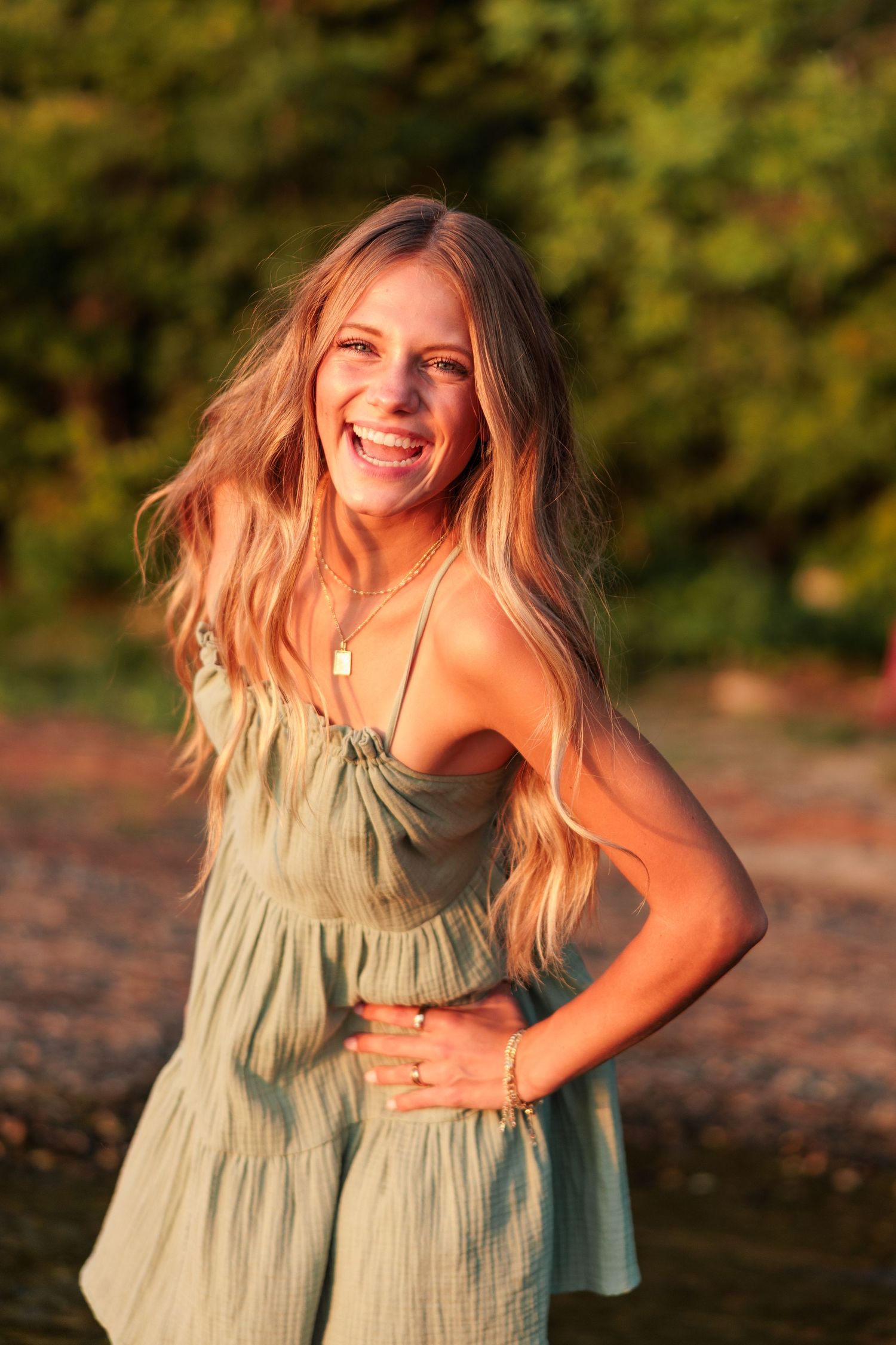Smiling blonde woman in green sundress poses outdoors in golden sunset light.