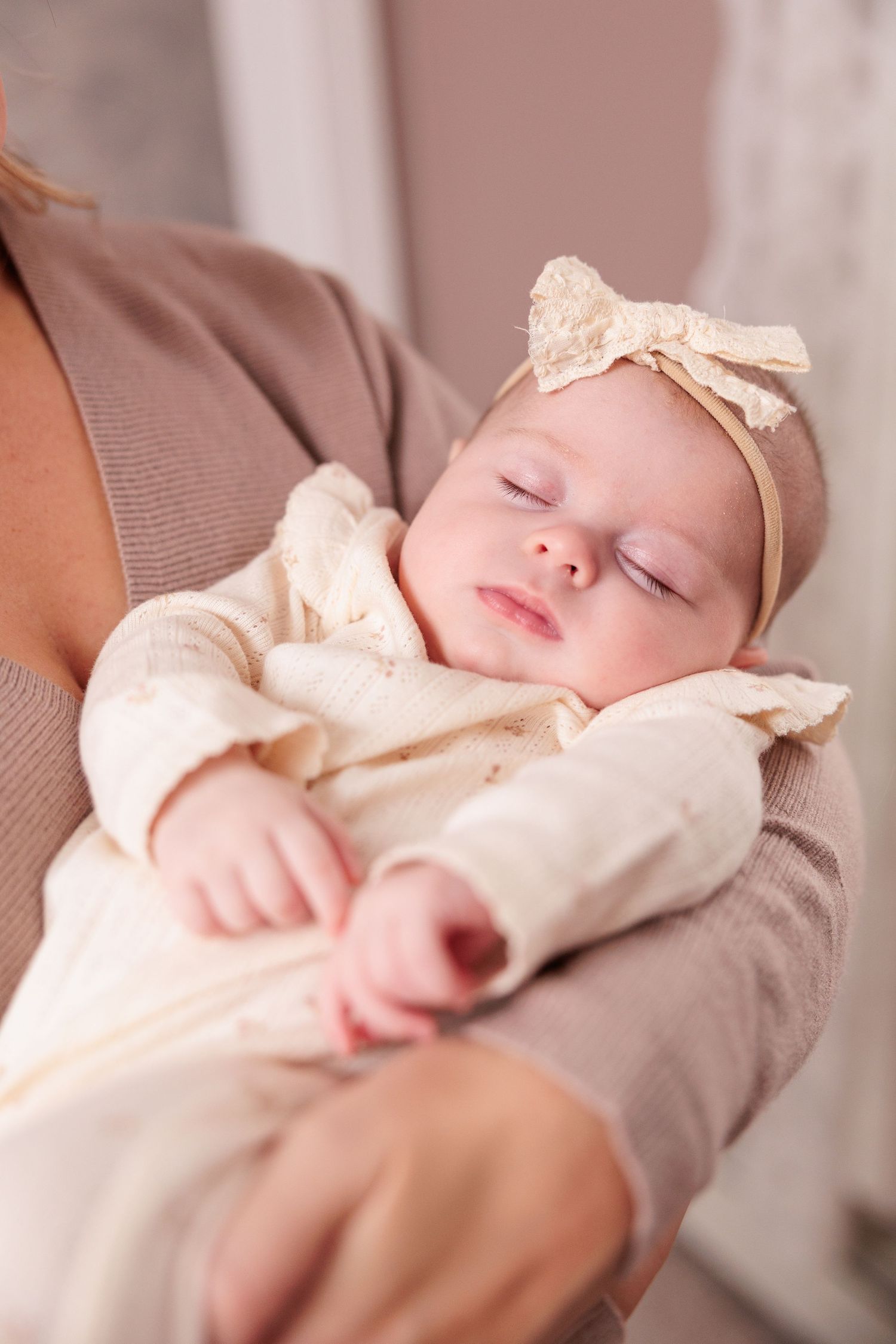A sleeping baby wearing a cream colored outfit with bow accessory rests peacefully.
