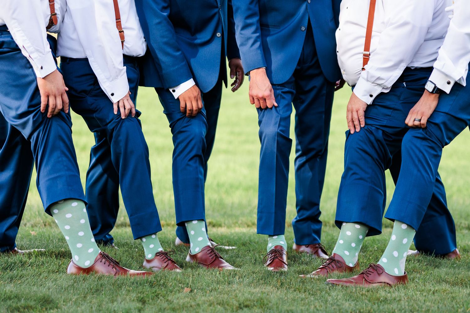 Row of groomsmen showing off matching mint green socks with navy blue suits and brown shoes.