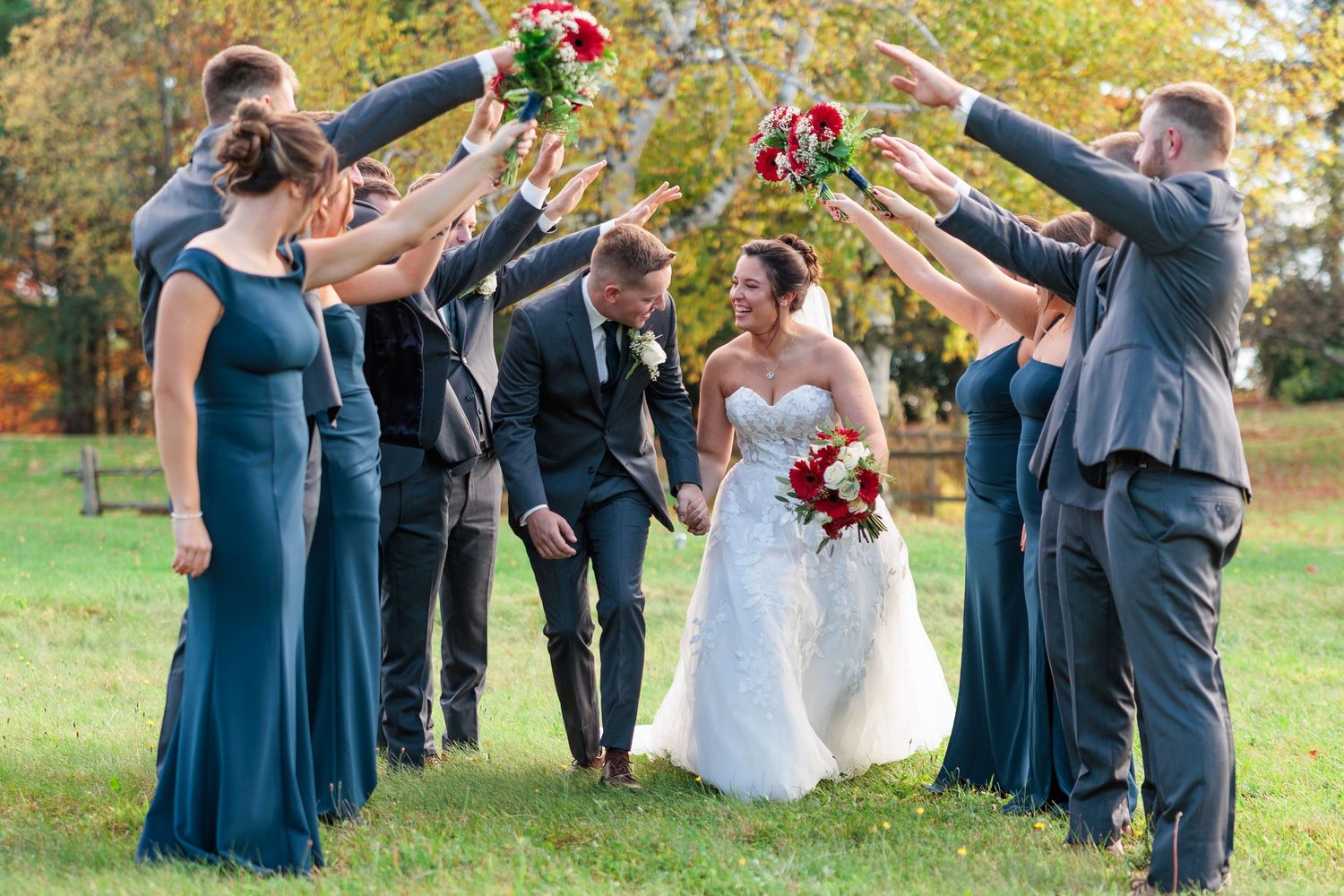 Wedding party celebrating with raised arms outdoors during fall season.