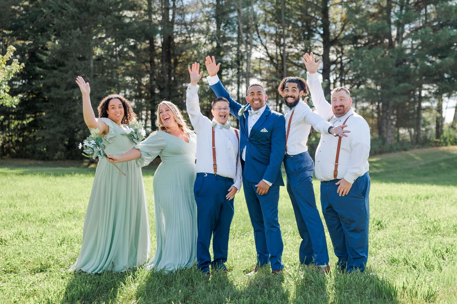 Joyful wedding party in mint green dresses and blue suits celebrating outdoors on grassy field.