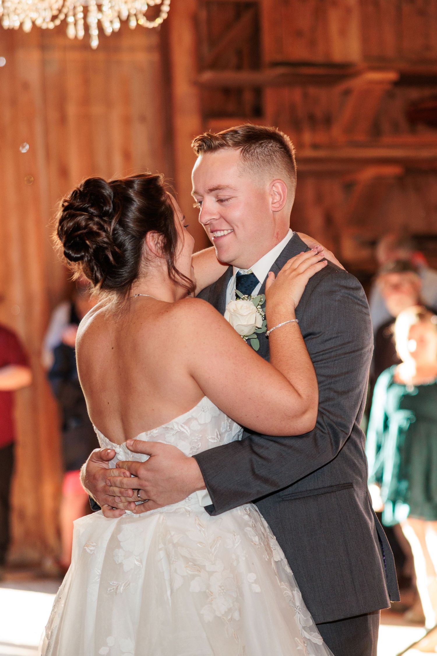 Bride and groom share an intimate first dance, embracing closely in a rustic barn wedding reception.