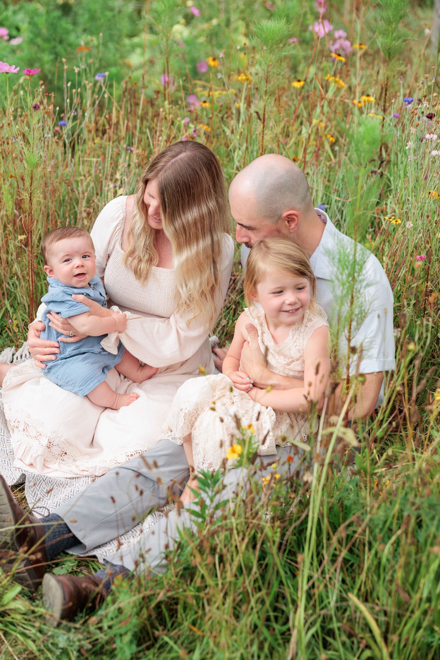 Happy family of four sitting together in a vibrant wildflower meadow on a sunny day.