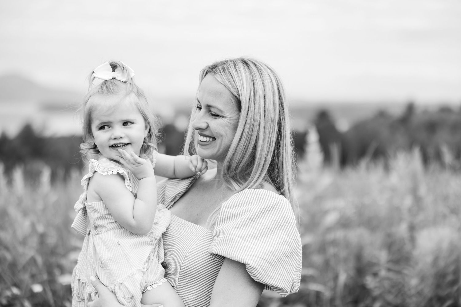 Black and white photo of a smiling mother holding her cheerful toddler daughter outdoors.