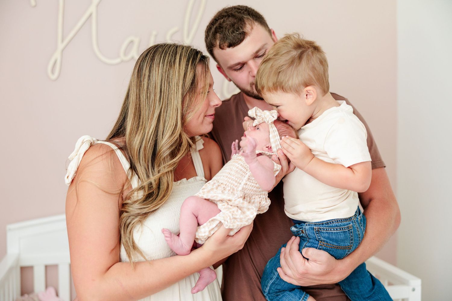 Loving family of four with parents and toddler son meeting their newborn baby girl.