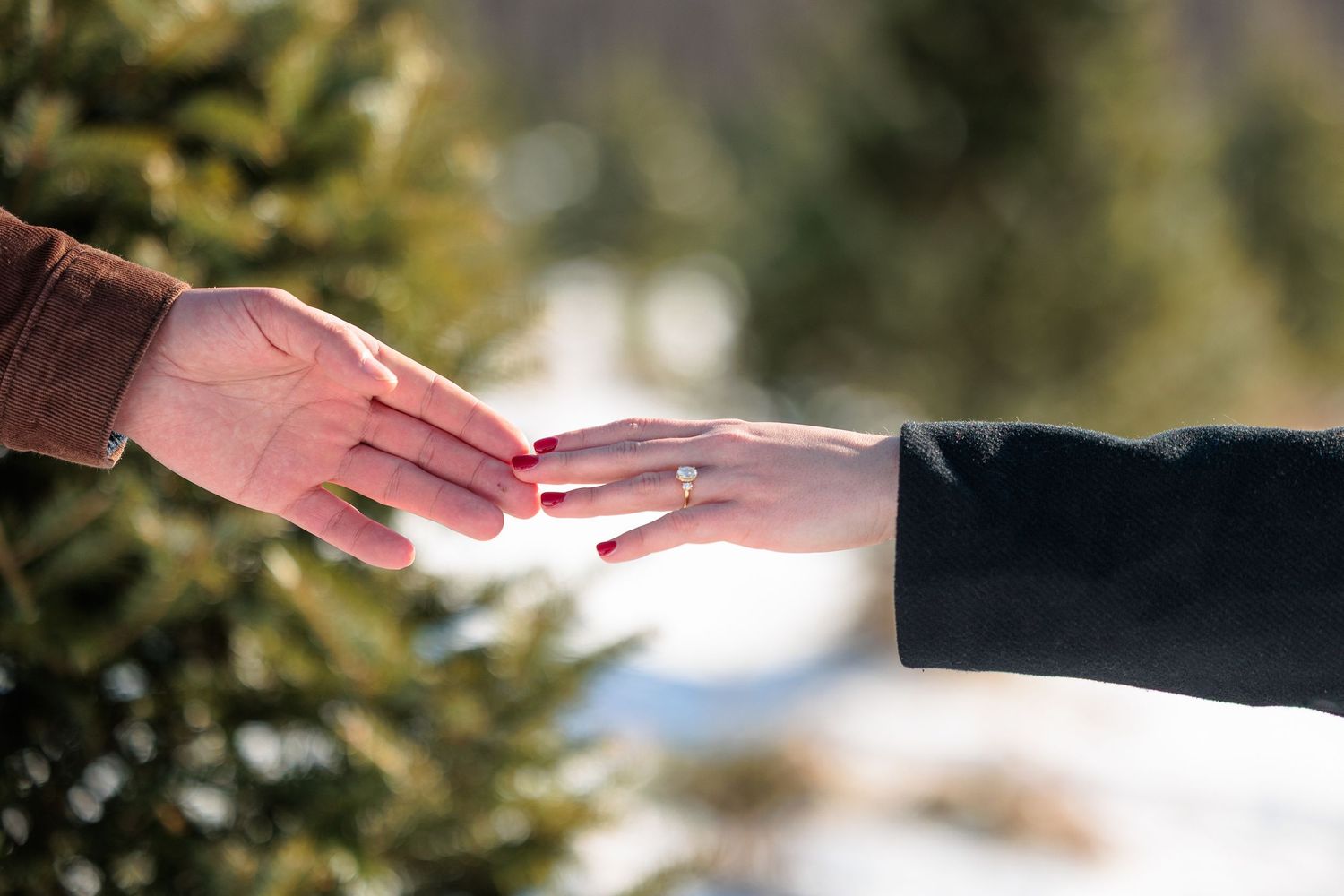 Close-up of an engaged couples hands touching, showing a diamond engagement ring outdoors in winter.