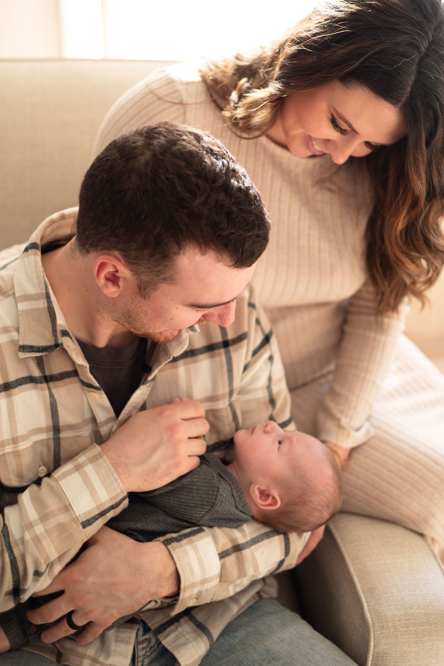 New parents lovingly admire their newborn baby while sitting together on a cozy couch at home.