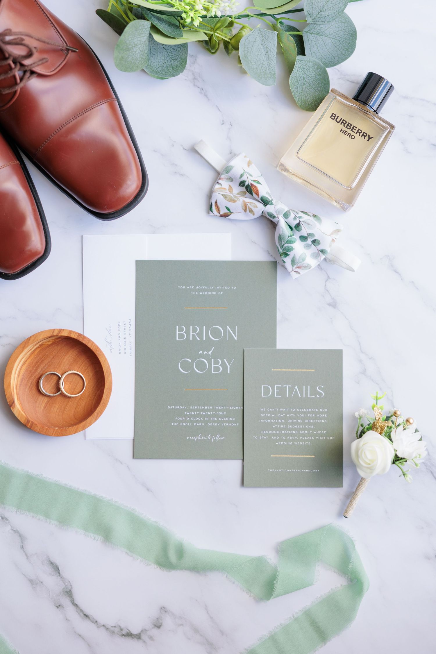 Wedding stationery suite in sage green with brown leather shoes and floral accents on marble.