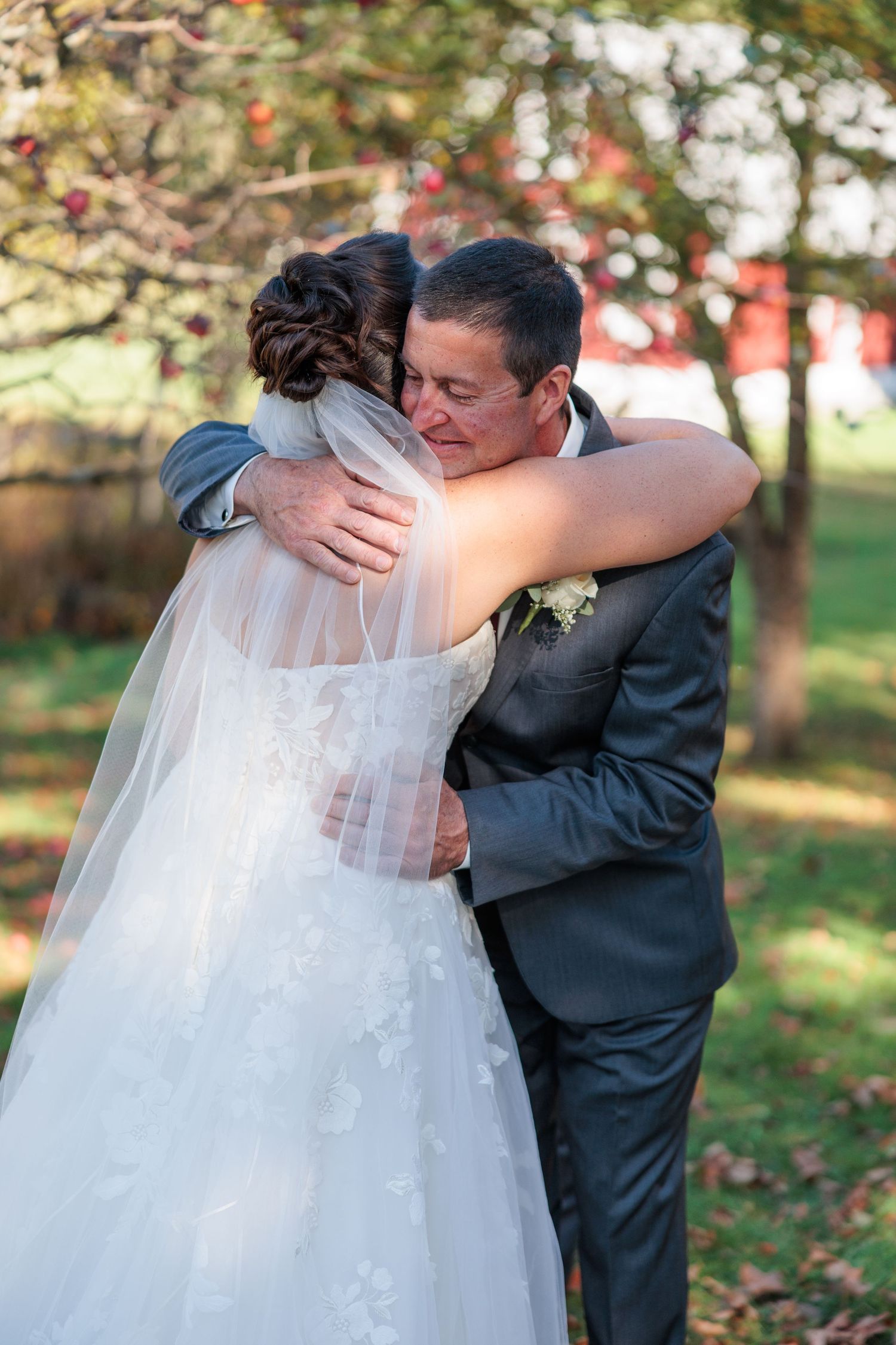 A romantic wedding moment captured outdoors with a flowing white veil and dark suit against an autumn backdrop.