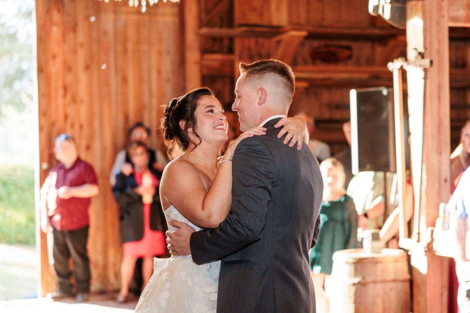 Romantic first dance moment inside rustic wooden barn with warm lighting.