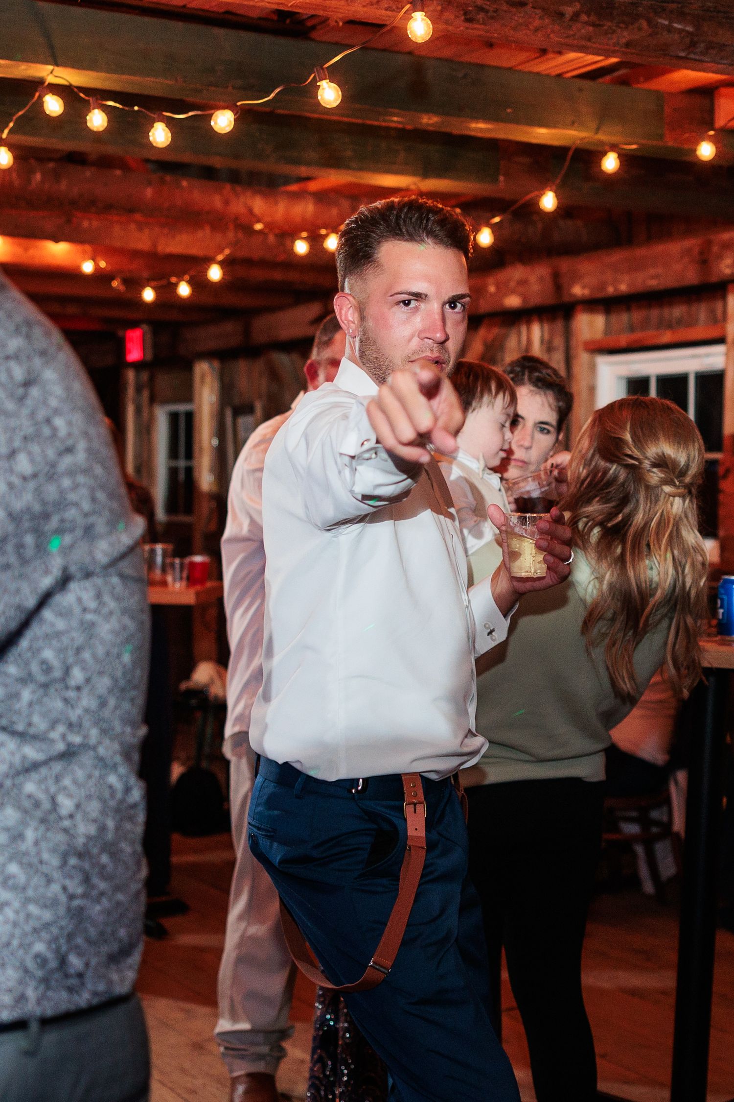 People dancing and enjoying themselves at a lively wedding reception with string lights overhead.