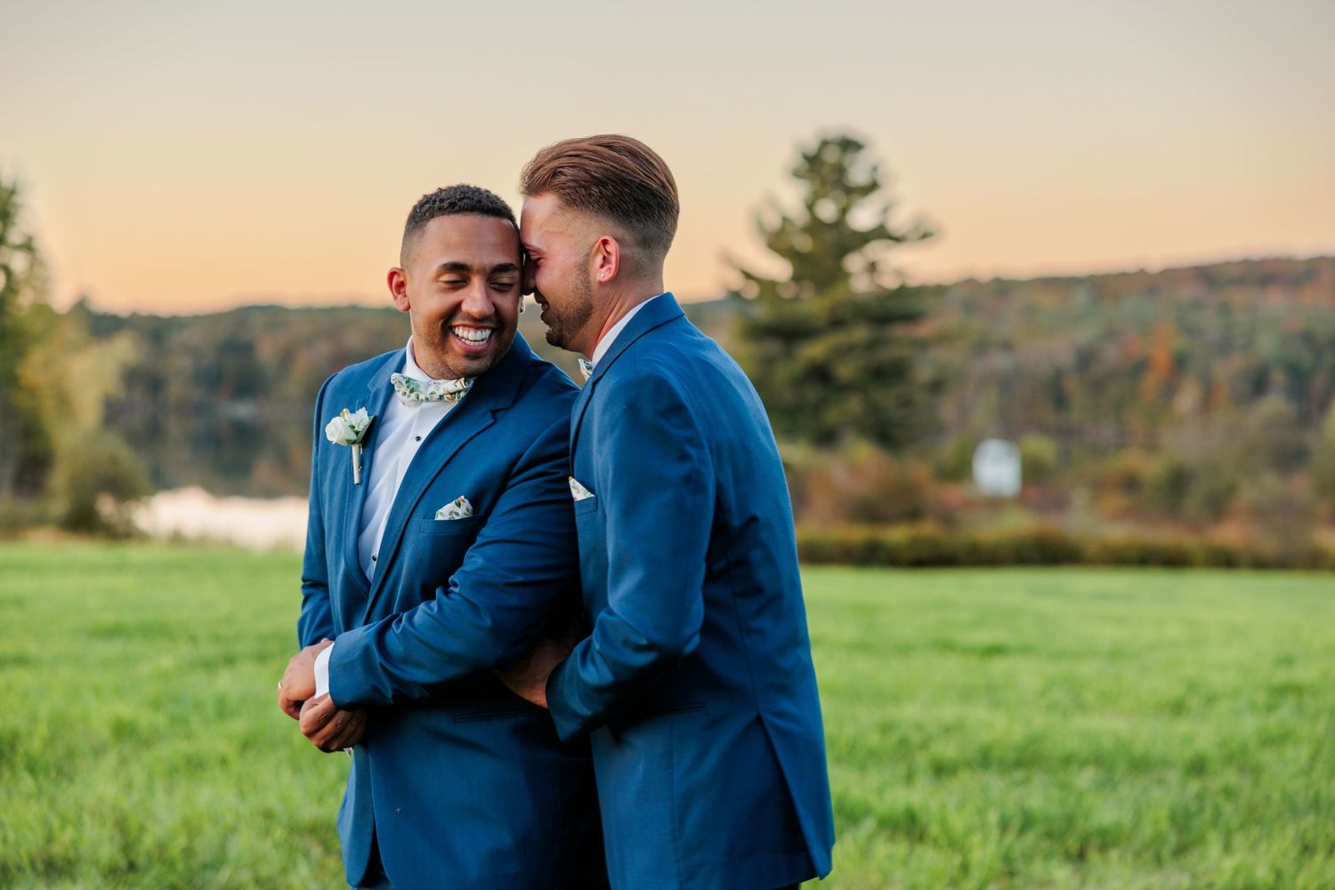 Two people in navy blue suits share a joyful moment in a sunlit field.