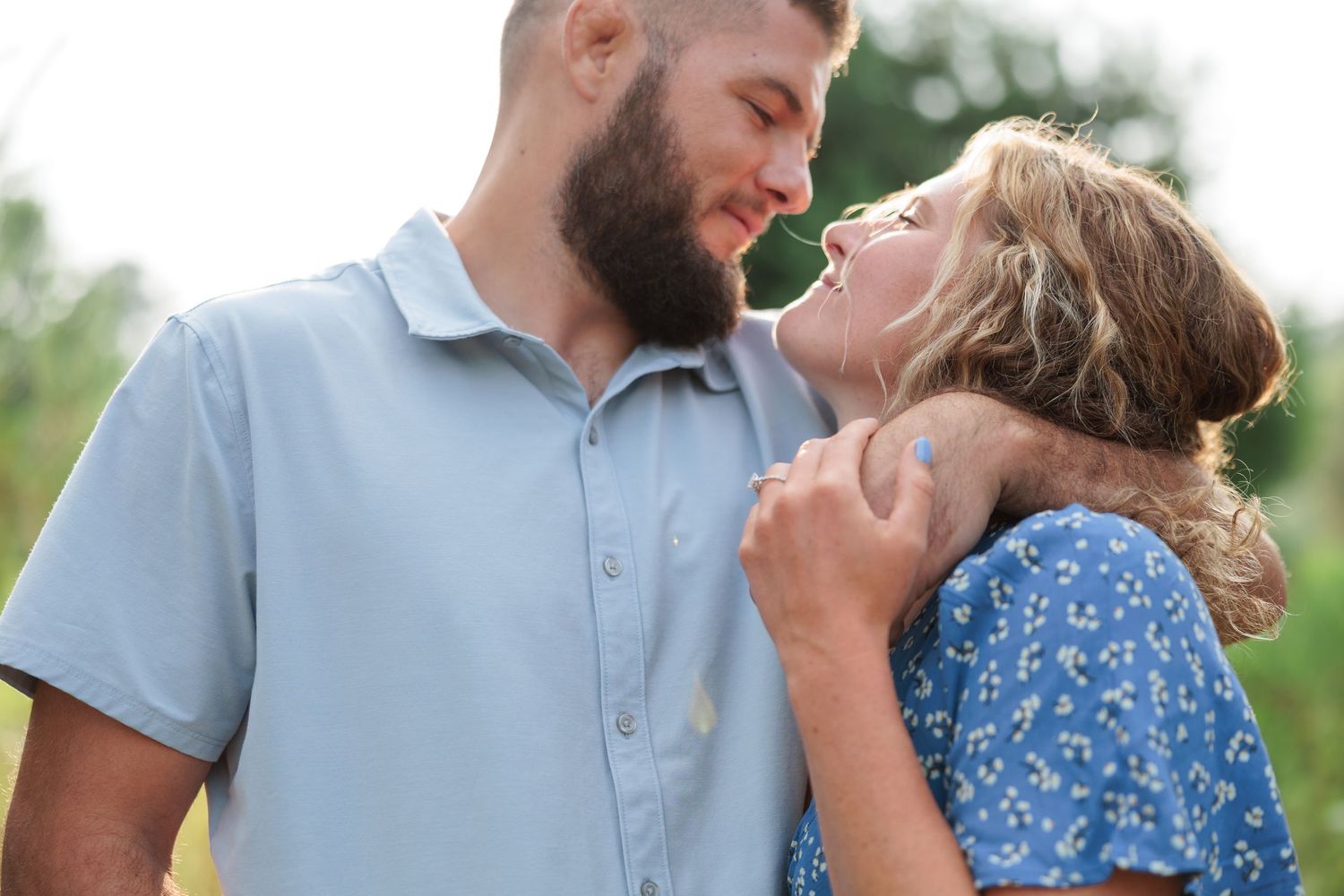 Happy couple nearly kissing outdoors in a green field, man in blue shirt and woman in floral dress.
