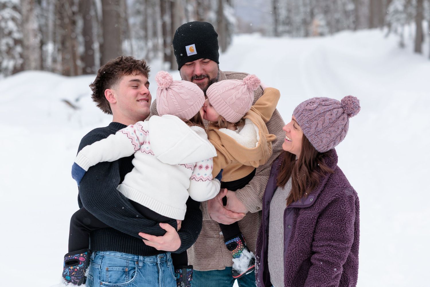 A joyful family with two babies laughs together in a snowy winter outdoor setting.