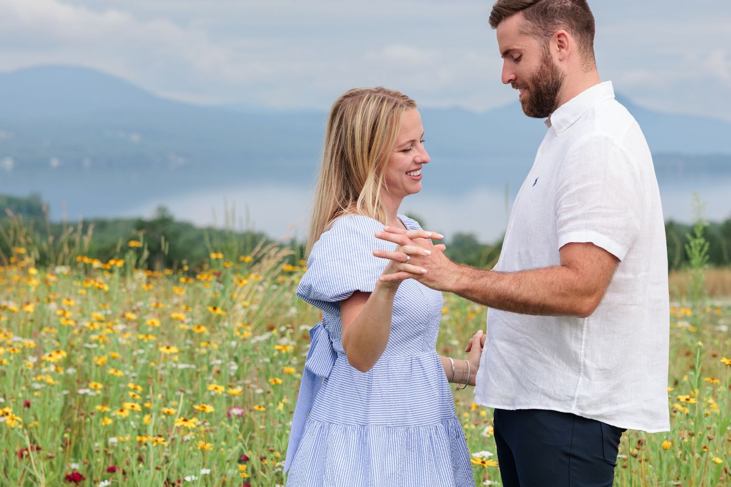 Happy couple holding hands in a colorful wildflower meadow with mountains visible in the background.