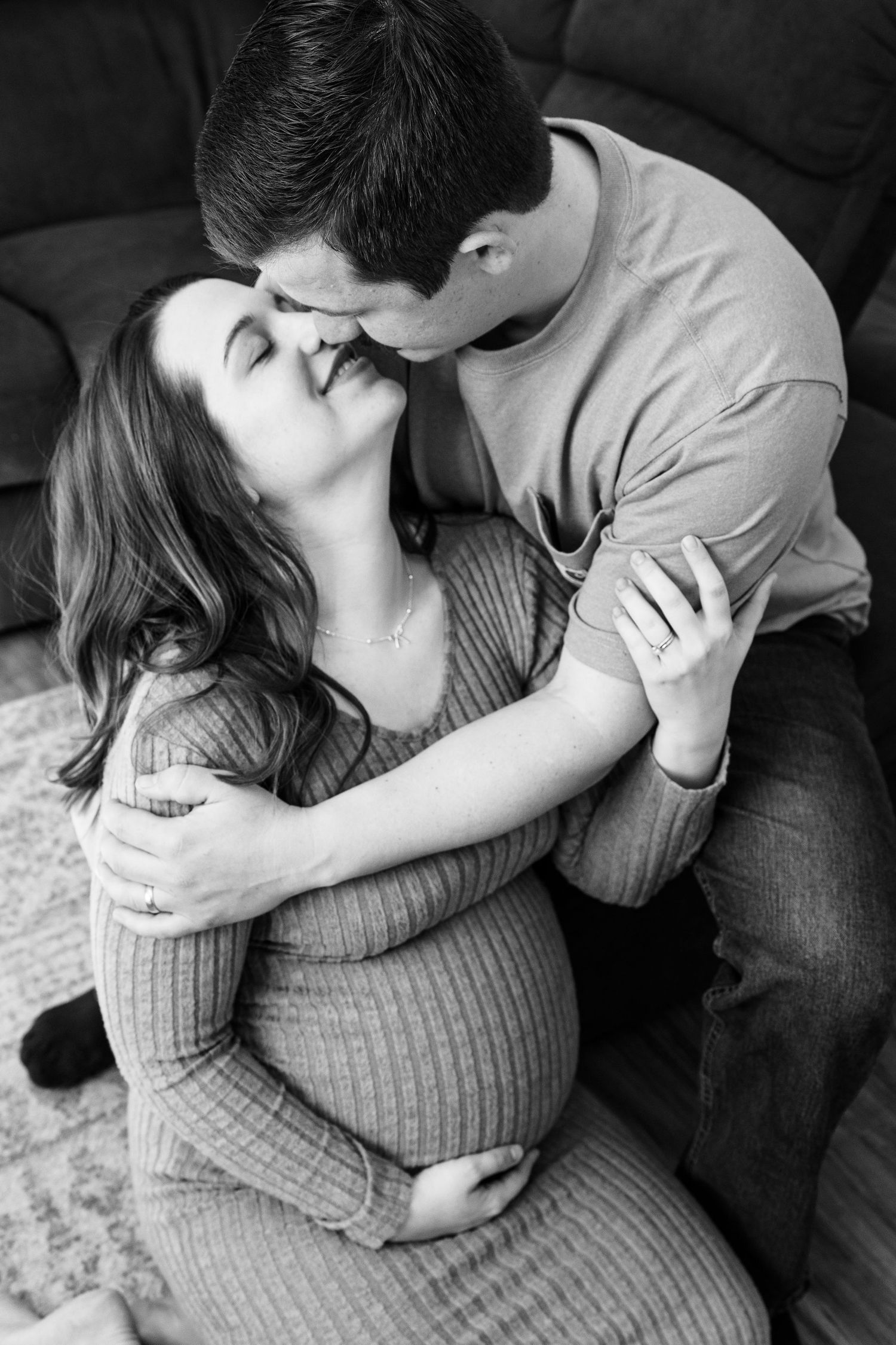 Black and white photo of couple sharing tender kiss with pregnant woman cradling her belly.