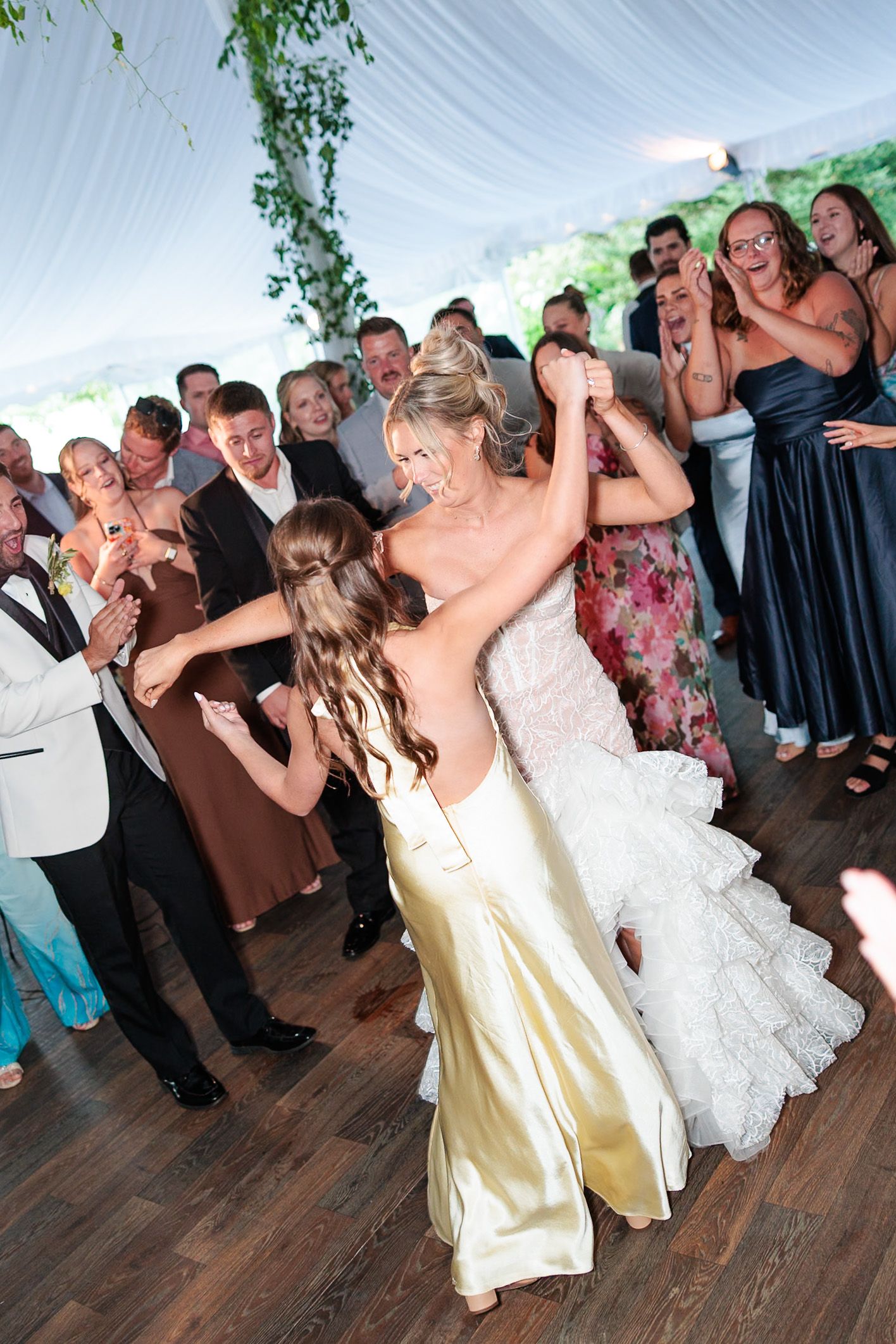 Bride and bridesmaid dancing together on the wedding reception dance floor under a white tent.
