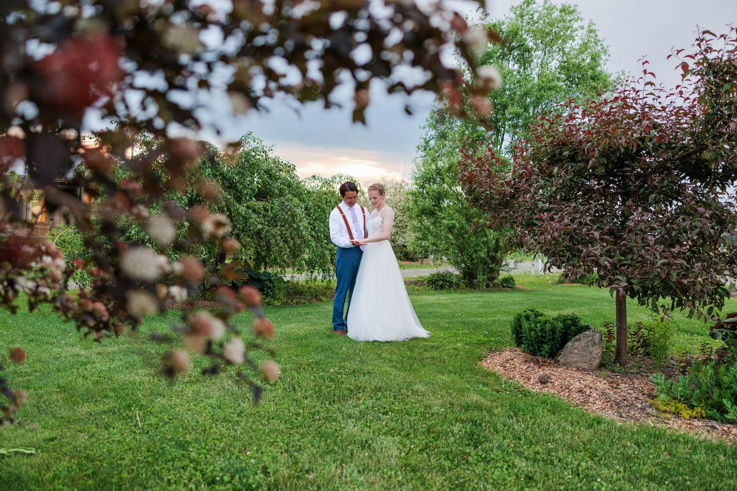 Bride and groom share tender moment surrounded by colorful trees at dusk.