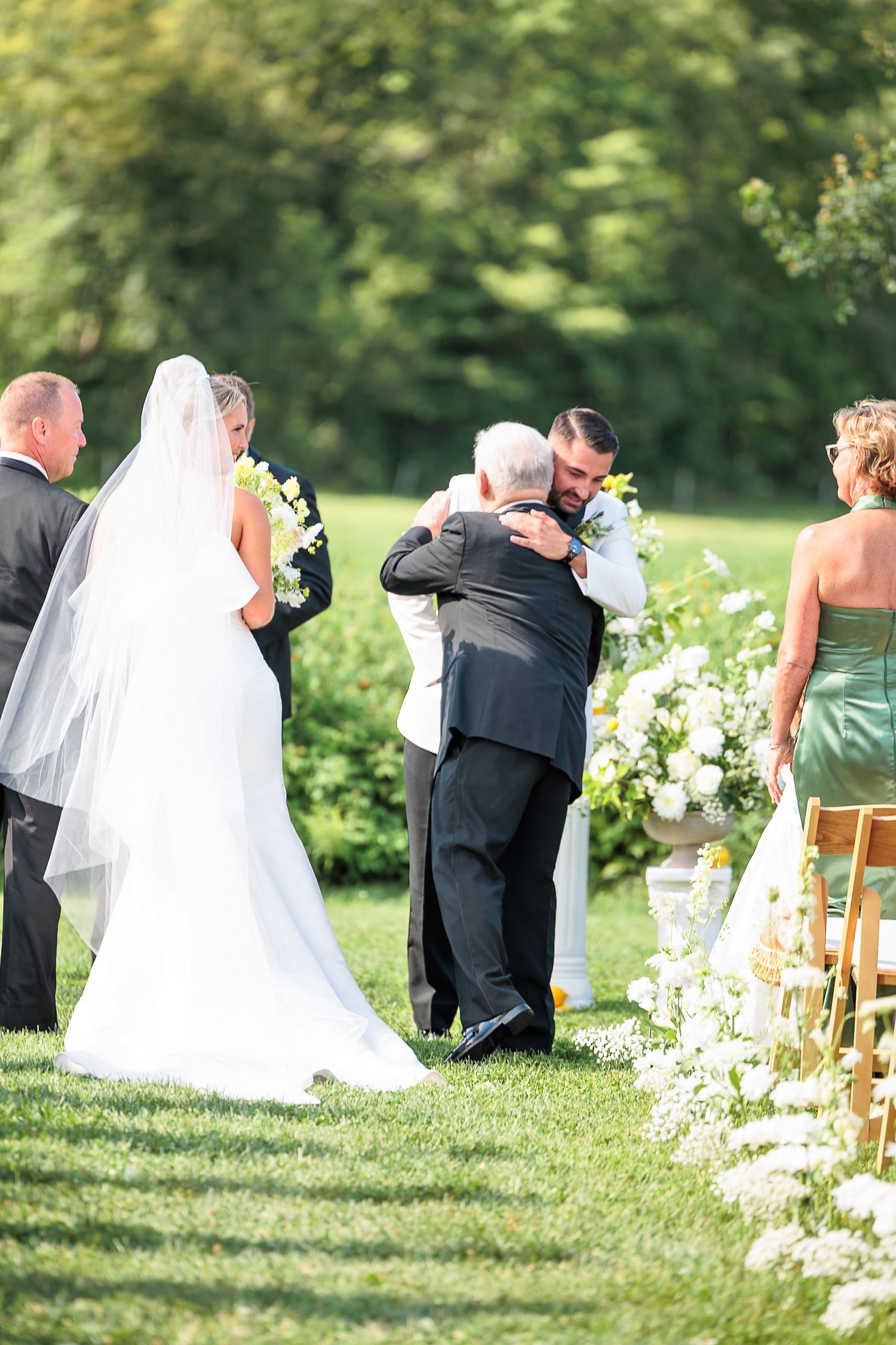 Emotional groom embracing father of the bride at the altar during touching outdoor wedding ceremony moment.