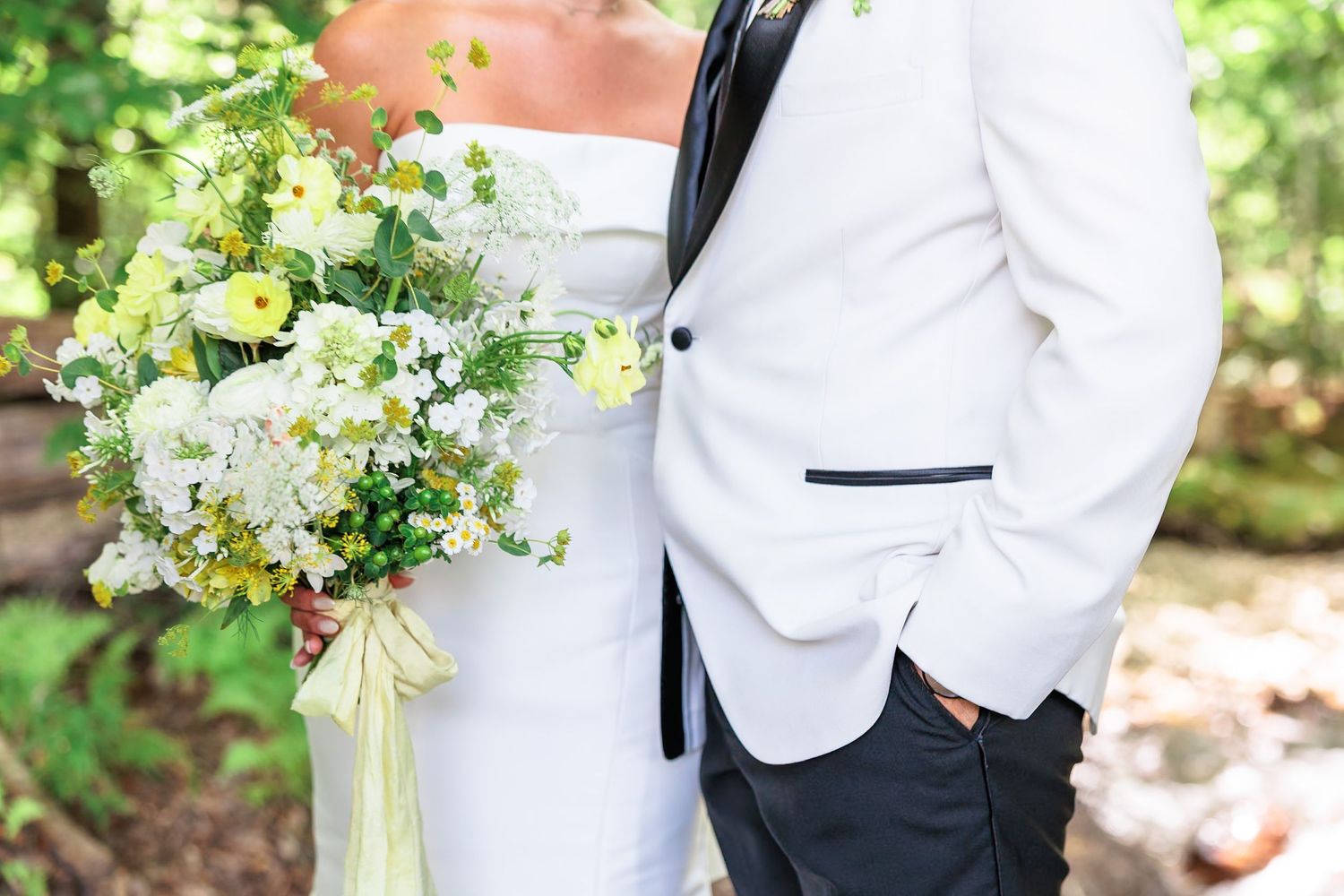 Bride and groom posing together with a lush white and yellow wildflower wedding bouquet in a garden.