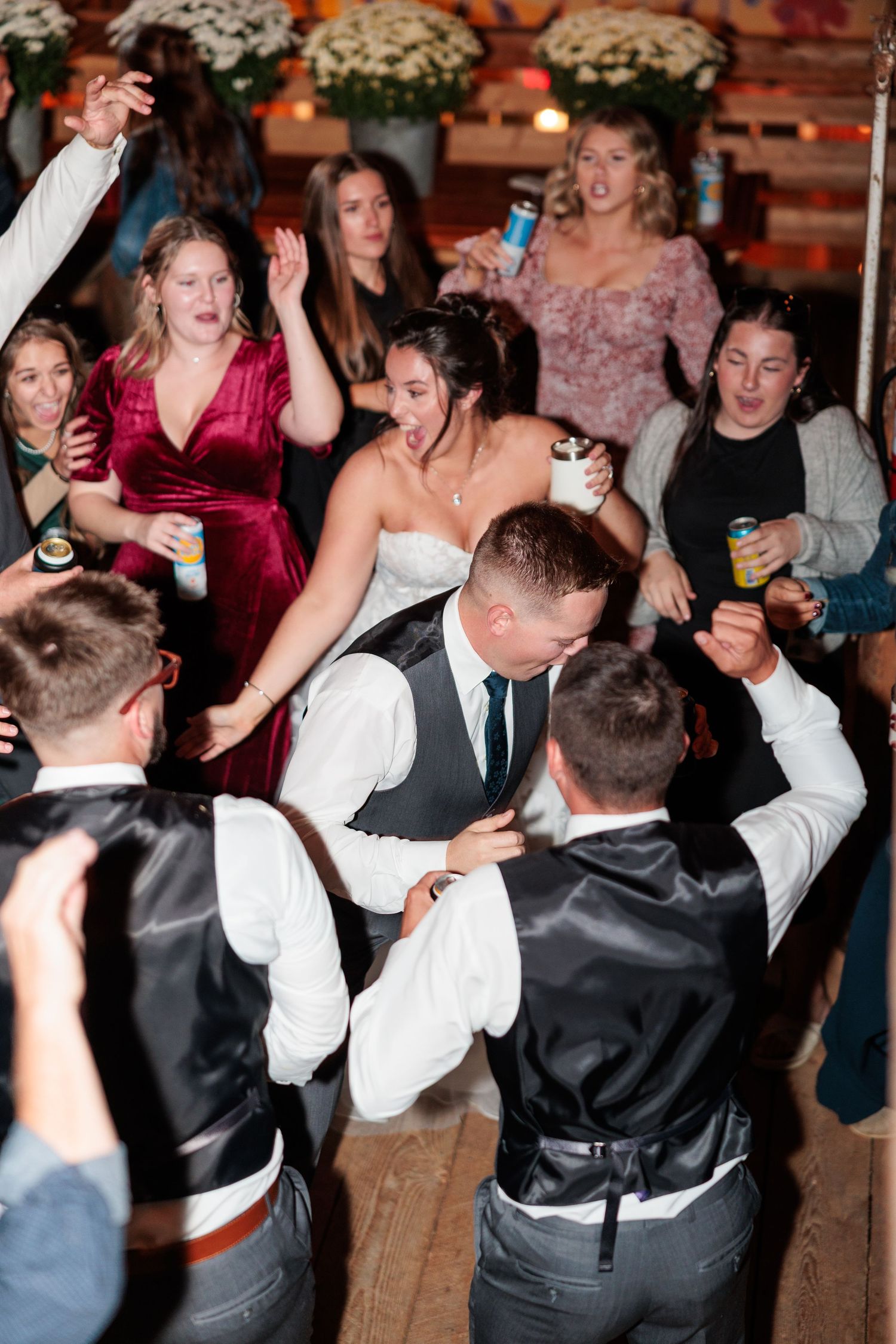 Groom lifts bride on a crowded dance floor as excited wedding guests celebrate around them.