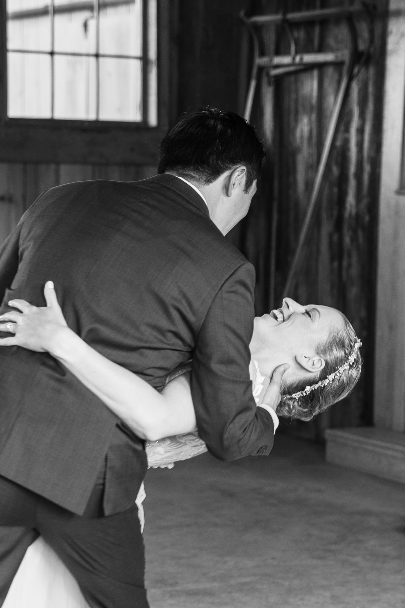 Black and white photo of groom dipping bride in white gown during their first dance at wedding reception.